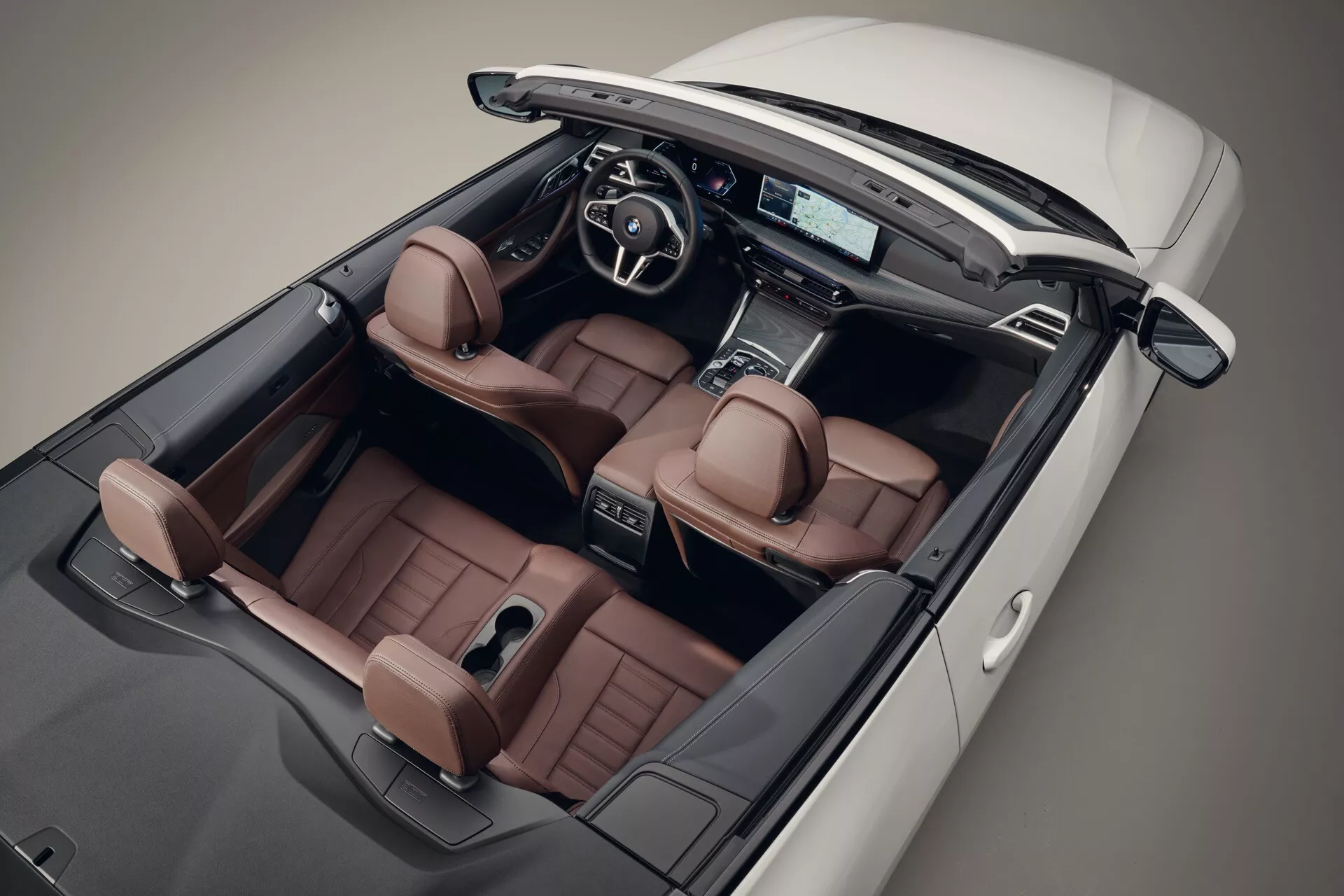 Vue aérienne de la BMW Série 4 décapotable 2024 avec toit abaissé montrant des sièges en cuir marron selle de luxe, un tableau de bord moderne avec un écran d'infodivertissement avancé, et un volant sportif multifonction