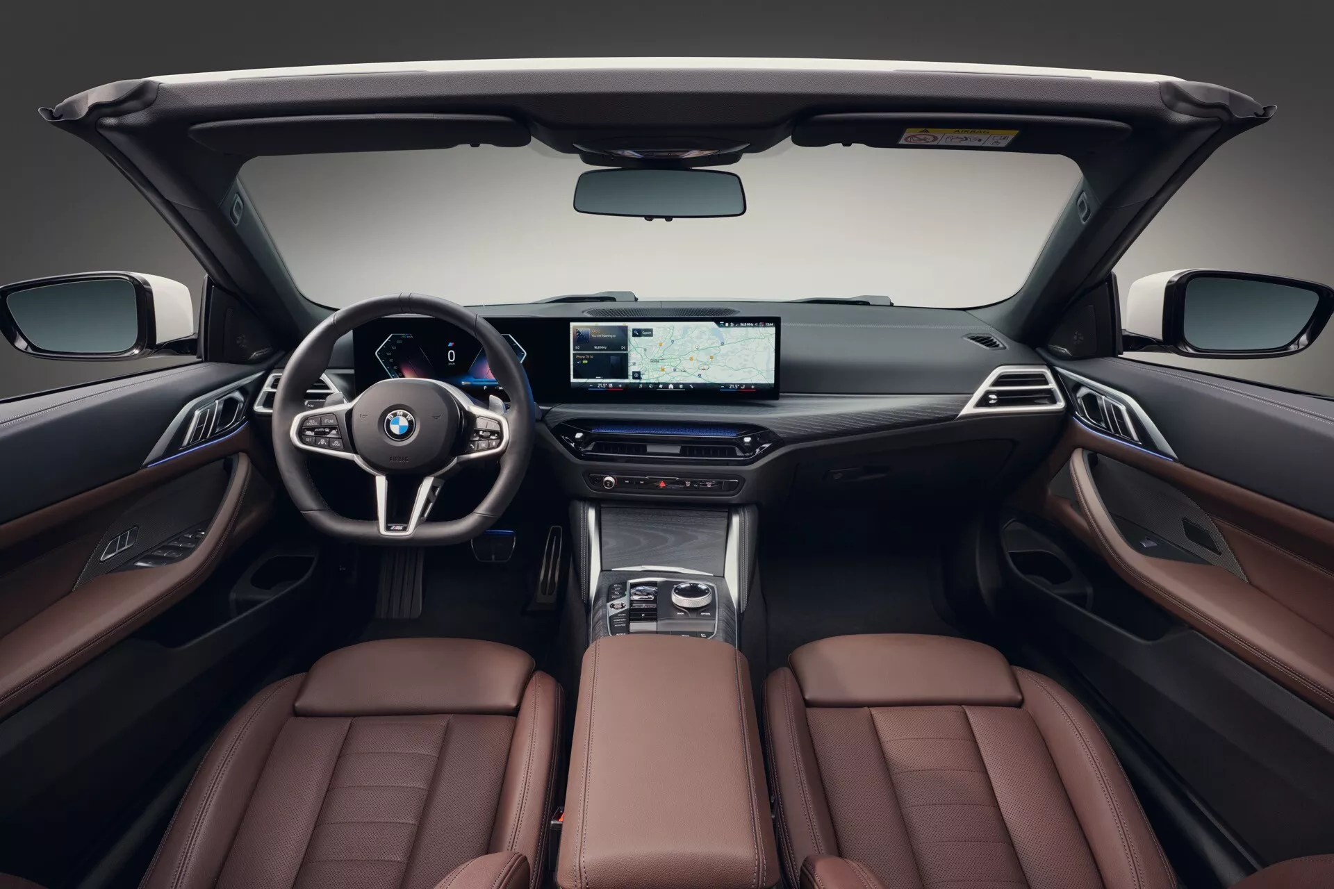 Vue intérieure de la BMW Série 4 2024 (G22-G23-G26-G82-G83 Facelift) montrant des sièges en cuir marron luxueux, un tableau de bord moderne avec écran large et un volant sportif, mettant en avant les caractéristiques haut de gamme et le design de l'habitacle.