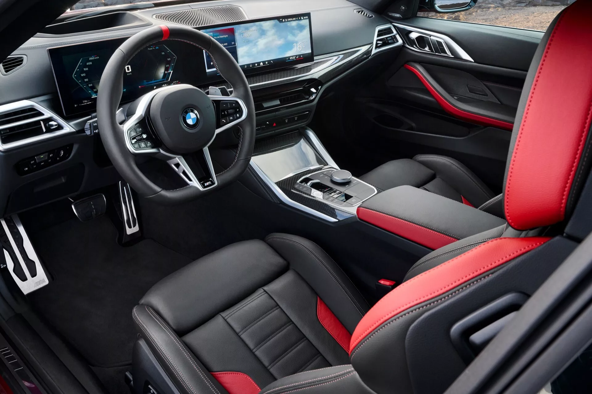 Vue intérieure de la BMW Série 4 (G22-G23-G26-G82-G83 Facelift) 2024 depuis le côté conducteur montrant des sièges sportifs en cuir noir avec des accents rouges, volant multifonction, tableau de bord élégant avec des écrans numériques et console centrale sophistiquée