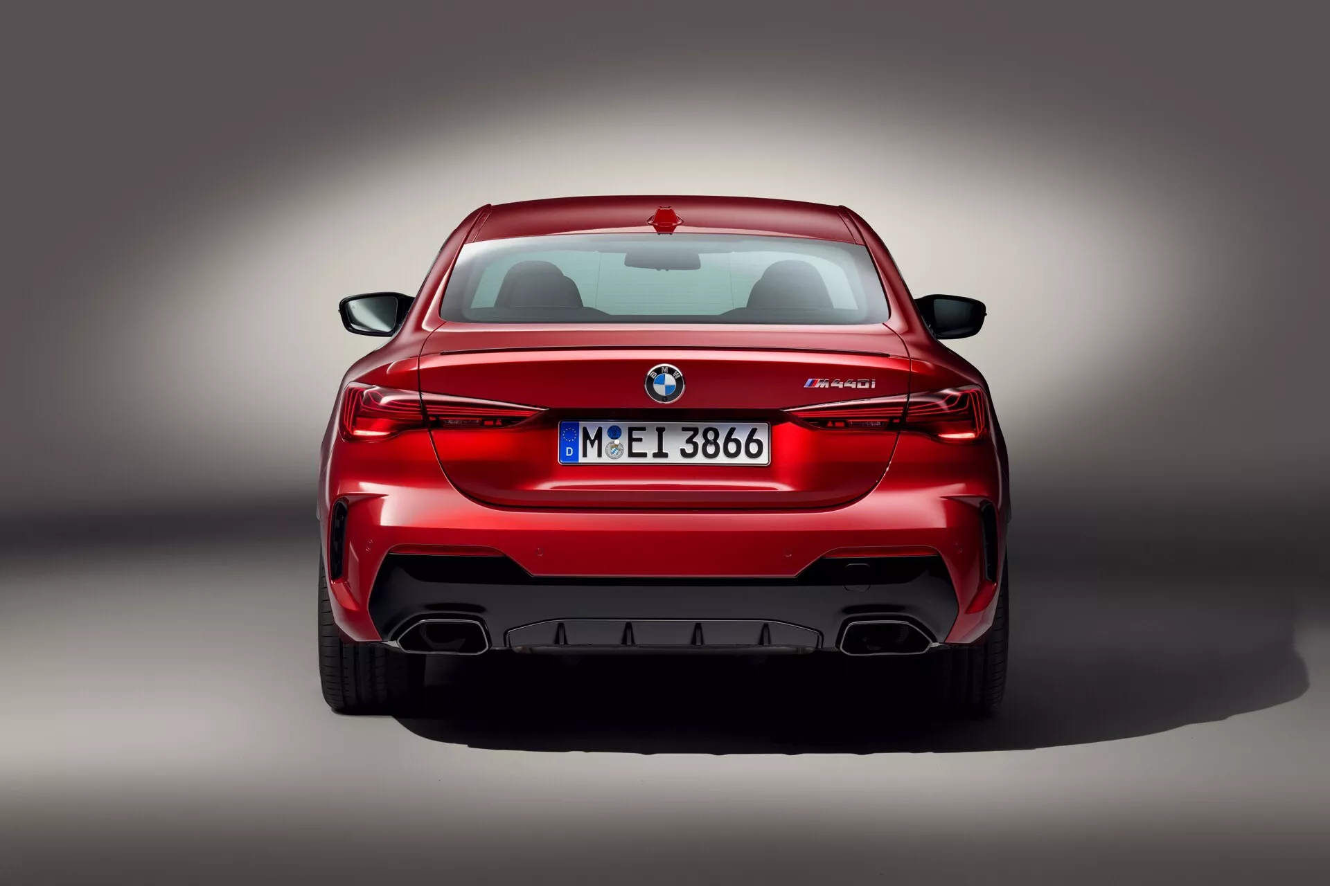 Vue arrière d'une BMW M5 rouge affichant des feux arrière en forme de L, un emblème, un badge M5 et des doubles sorties d'échappement avec diffuseur, photo en studio avec éclairage professionnel
