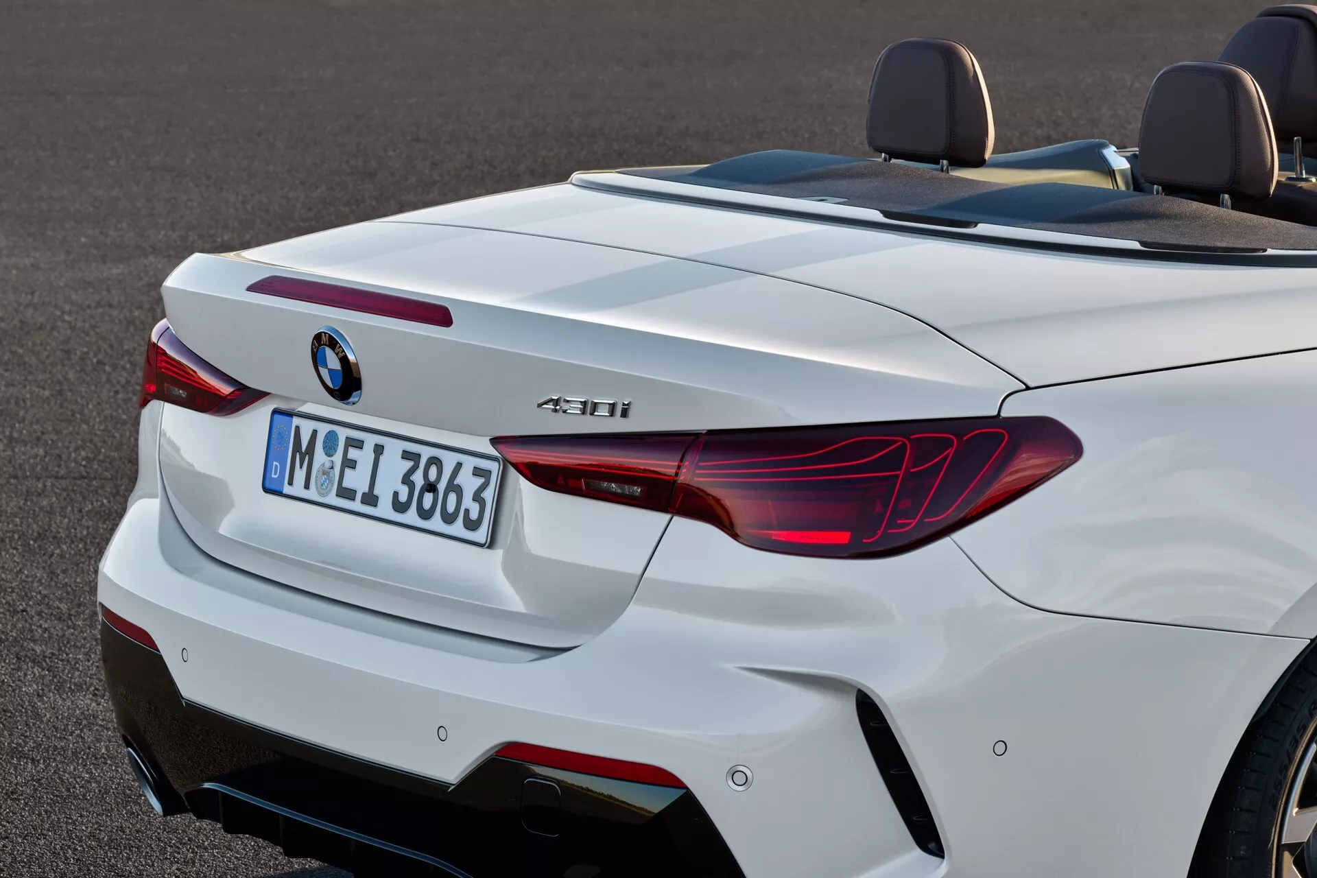 Vue arrière d'une BMW Série 4 Cabriolet blanche (restylage 2024) présentant des feux arrière LED en forme de L, des doubles sorties d'échappement et un diffuseur sportif, avec un focus clair sur sa silhouette arrière aérodynamique et des fonctionnalités technologiques telles que les capteurs de stationnement arrière