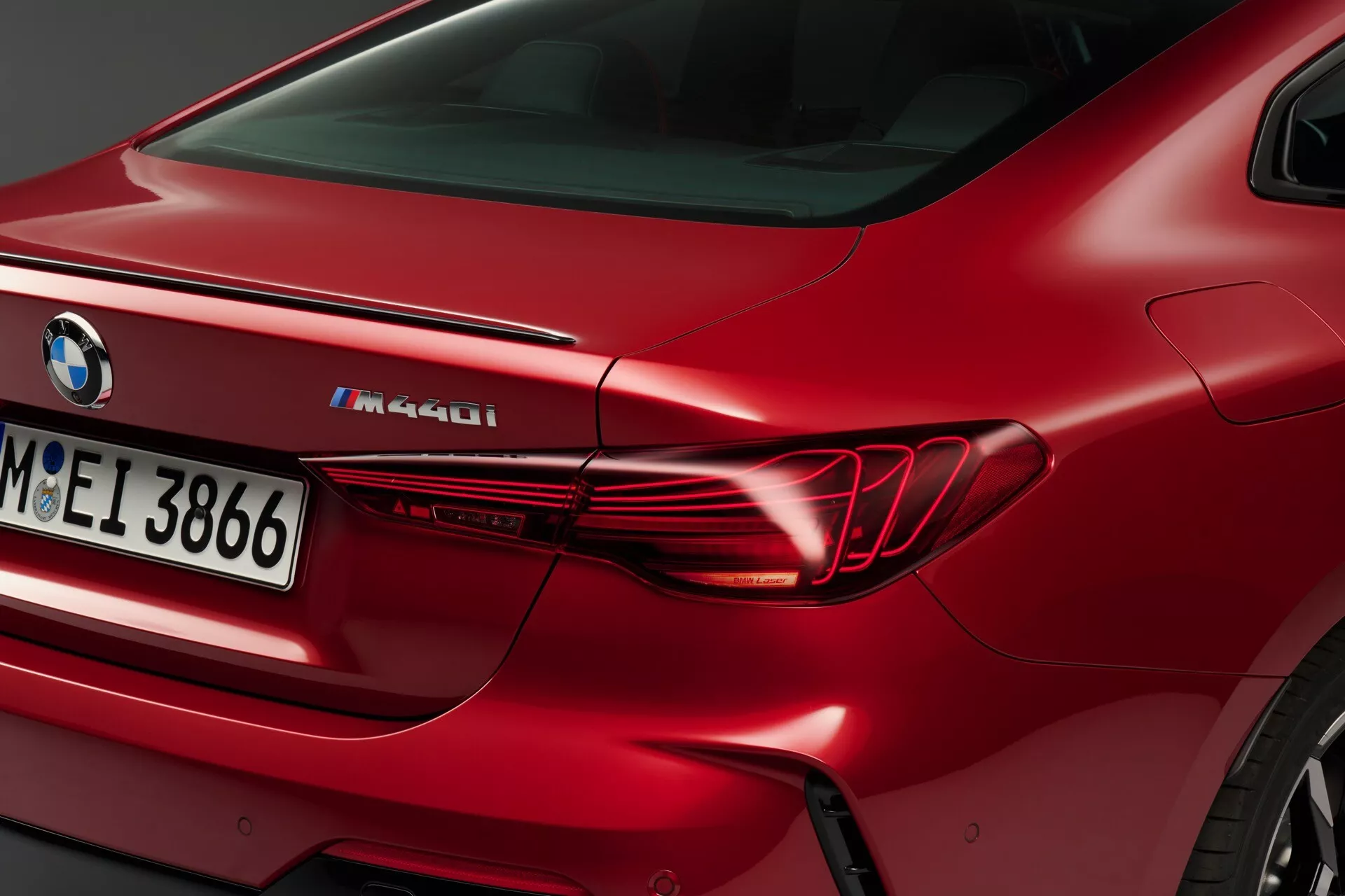 Vue rapprochée du quart arrière d'une BMW M440i 2024 rouge, montrant le design élégant horizontal du feu arrière, le garde-boue arrière sculpté et la désignation M Performance sur le couvercle du coffre.