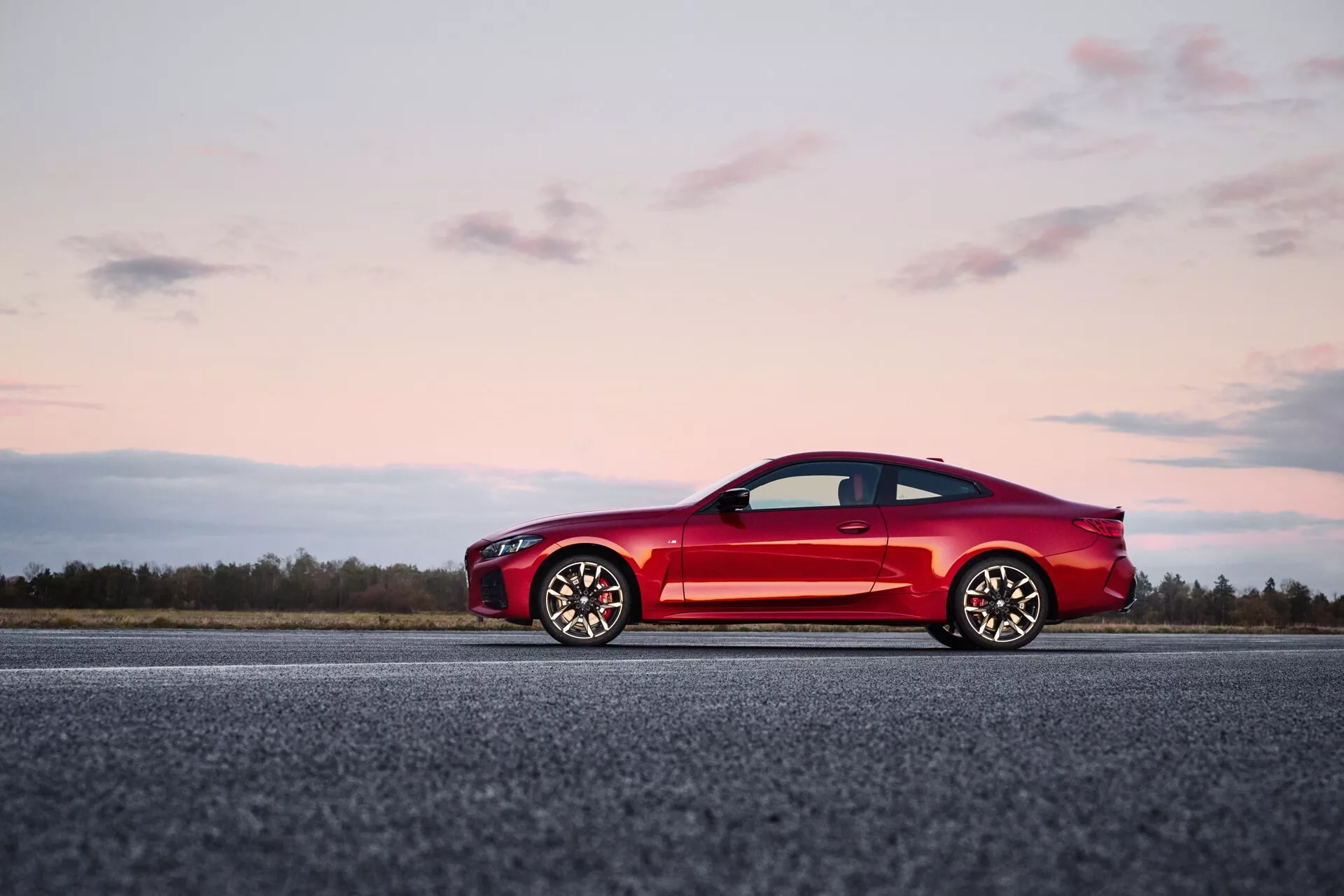 Coupé sportif rouge BMW Série 4 (G22-G23-G26-G82-G83 Facelift) à deux portes sur piste d'atterrissage avec ciel crépusculaire en fond, soulignant un design élégant, aérodynamique avec de grandes roues en alliage à multiples rayons et des caractéristiques modernes.