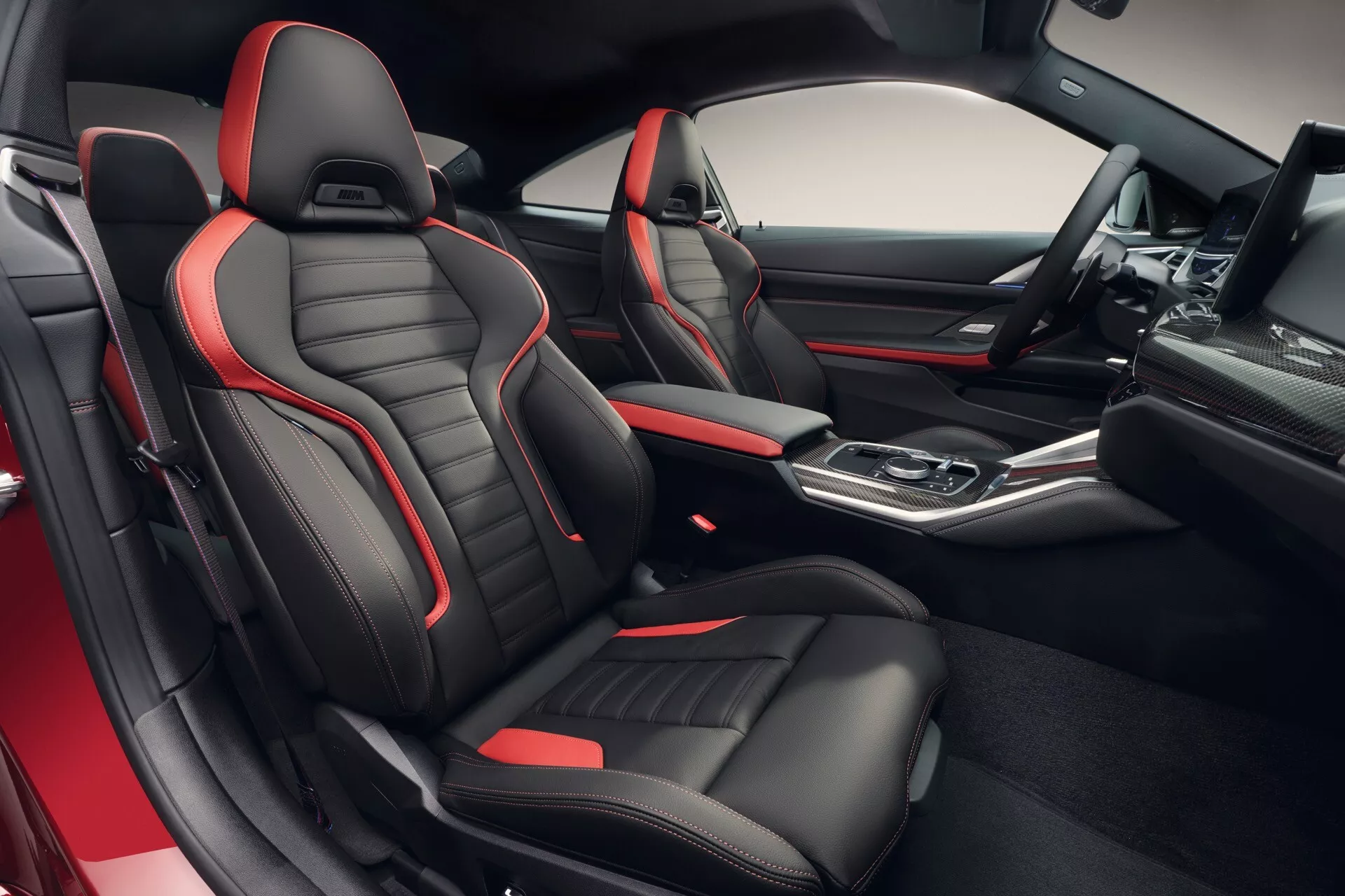 Vue intérieure de la BMW Série 4 2024 (G22-G23-G26-G82-G83 Facelift) montrant des sièges sportifs avec garniture noire et rouge, une console centrale de haute technologie avec sélecteur de vitesse automatique et des fonctionnalités premium du tableau de bord