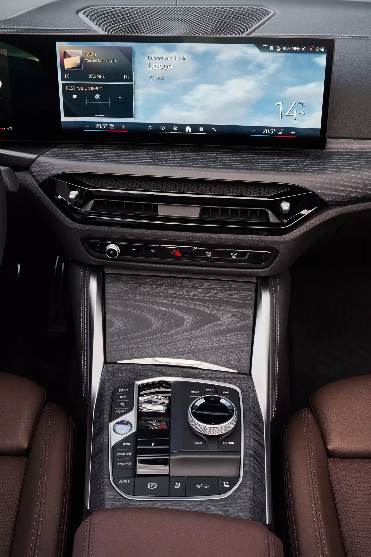Vue en plongée sur la console centrale de la BMW Série 4 2024 (G22-G23-G26-G82-G83 lifting) montrant l'écran d'infodivertissement, les grilles de ventilation, le placage en bois brillant et le sélecteur de vitesse électrique dans un intérieur de voiture de luxe