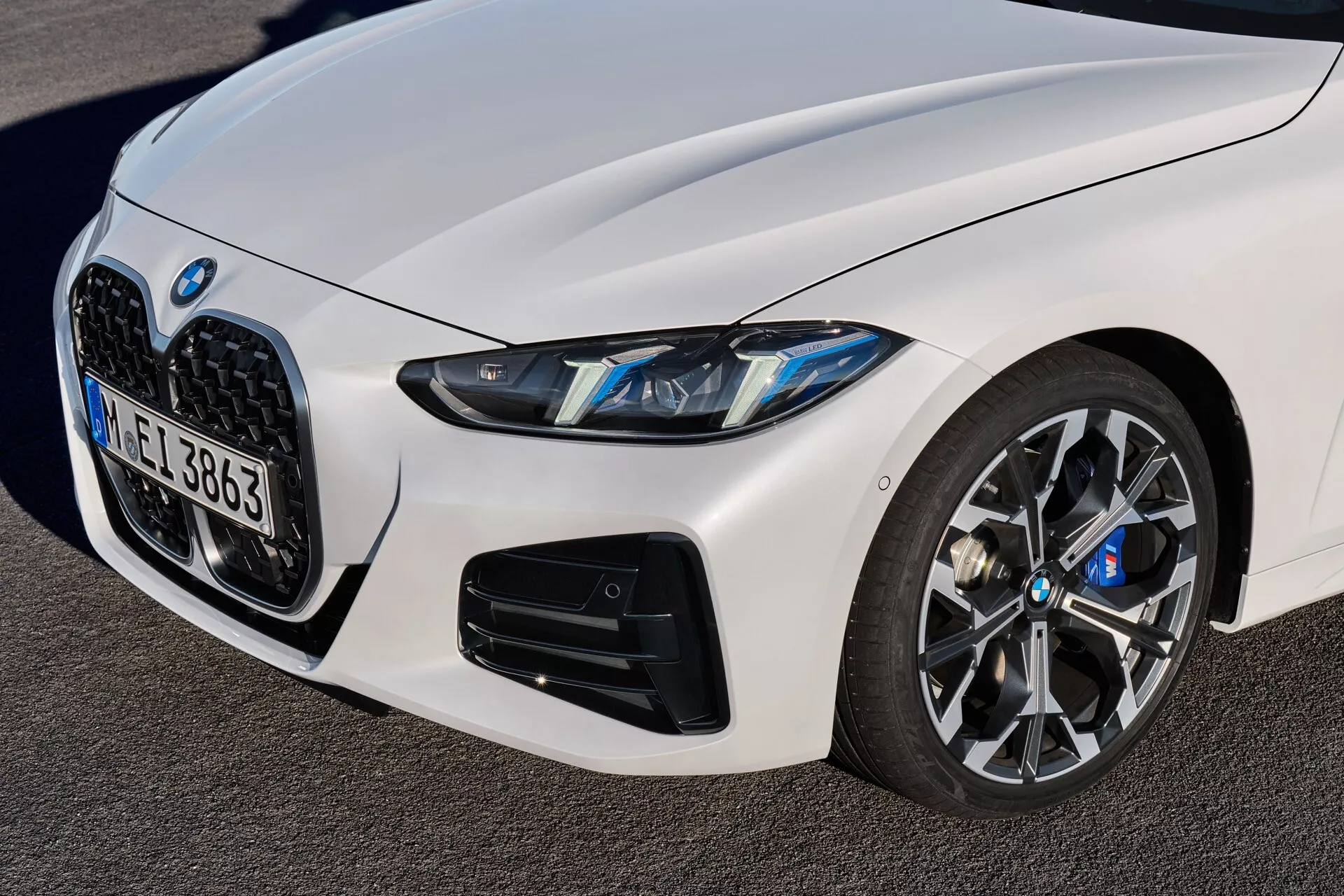 Vue détaillée de la BMW Série 4 2024 (G22-G23-G26-G82-G83 lifting) montrant le quadrant avant gauche, avec une grille en forme de rein, des phares LED, de grandes prises d'air orientées performance sur le pare-chocs inférieur et une roue à multiples branches avec un système de freinage avancé, le tout sous un angle bas et ascendant soulignant les éléments de design sportif et luxueux de la voiture.