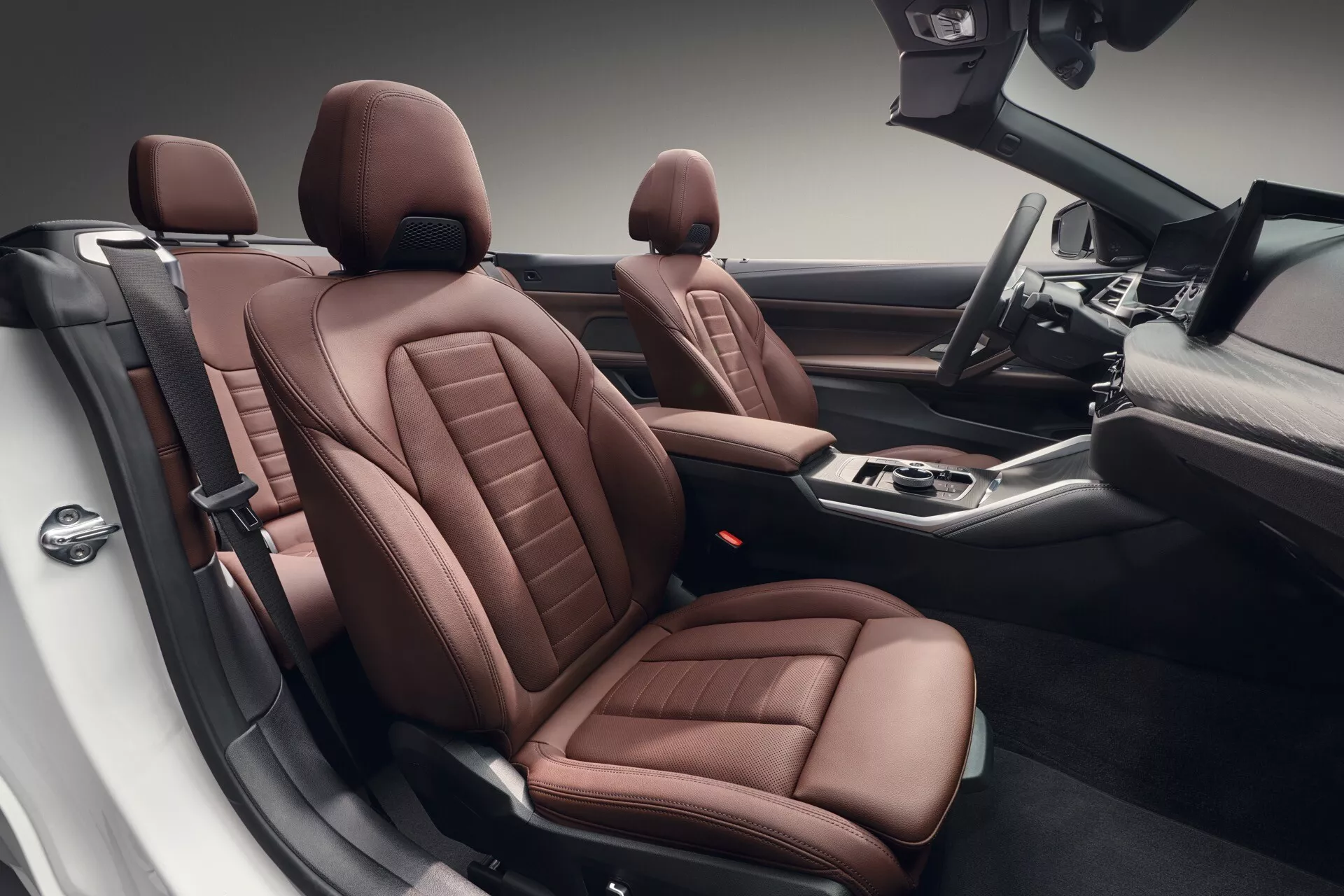 Vue intérieure d'une BMW Série 4 de 2024 (G22-G23-G26-G82-G83 lifting) offrant une perspective haute sur des sièges en cuir marron luxueux avec coutures complexes, des commandes avancées sur la console centrale, et un design d'habitacle spacieux soulignant un artisanat sophistiqué et des commodités technologiques modernes.