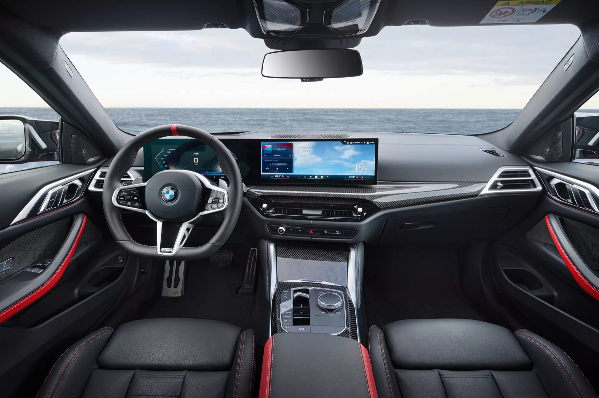 Vue intérieure de la BMW Série 4 2024 (G22-G23-G26-G82-G83 restylée) montrant le tableau de bord sportif, le volant multifonctions avec palettes de changement de vitesse, le combiné d'instruments numérique et l'écran d'infodivertissement large en haute résolution depuis une perspective du siège arrière