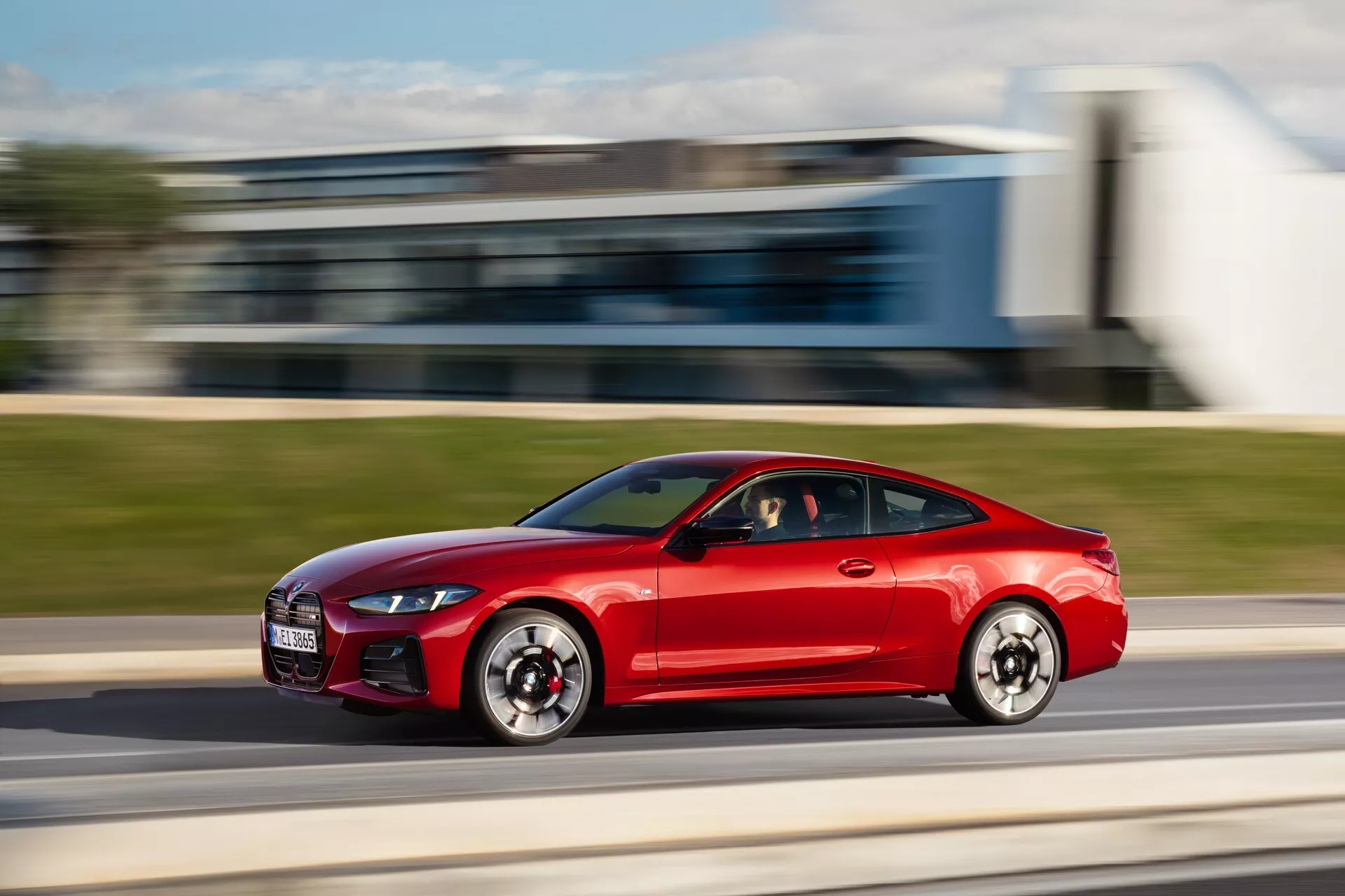 Coupé sportif rouge BMW Série 4 (G22-G23-G26-G82-G83 Facelift) en mouvement, vue de côté avec technique de panoramique montrant design aérodynamique, lumières diurnes LED et prises d'air de performance larges.