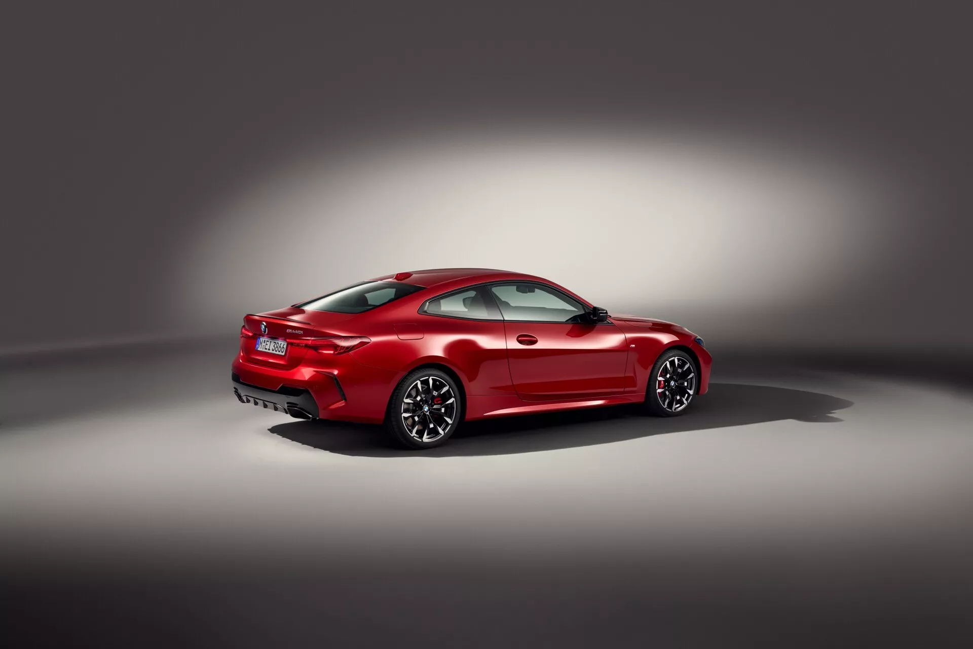 Coupé sportif rouge BMW Série 4 (G22-G23-G26-G82-G83 Facelift) avec jantes en alliage à rayons multiples, finition brillante et feux arrière LED, vu sous un angle arrière de trois quarts en studio