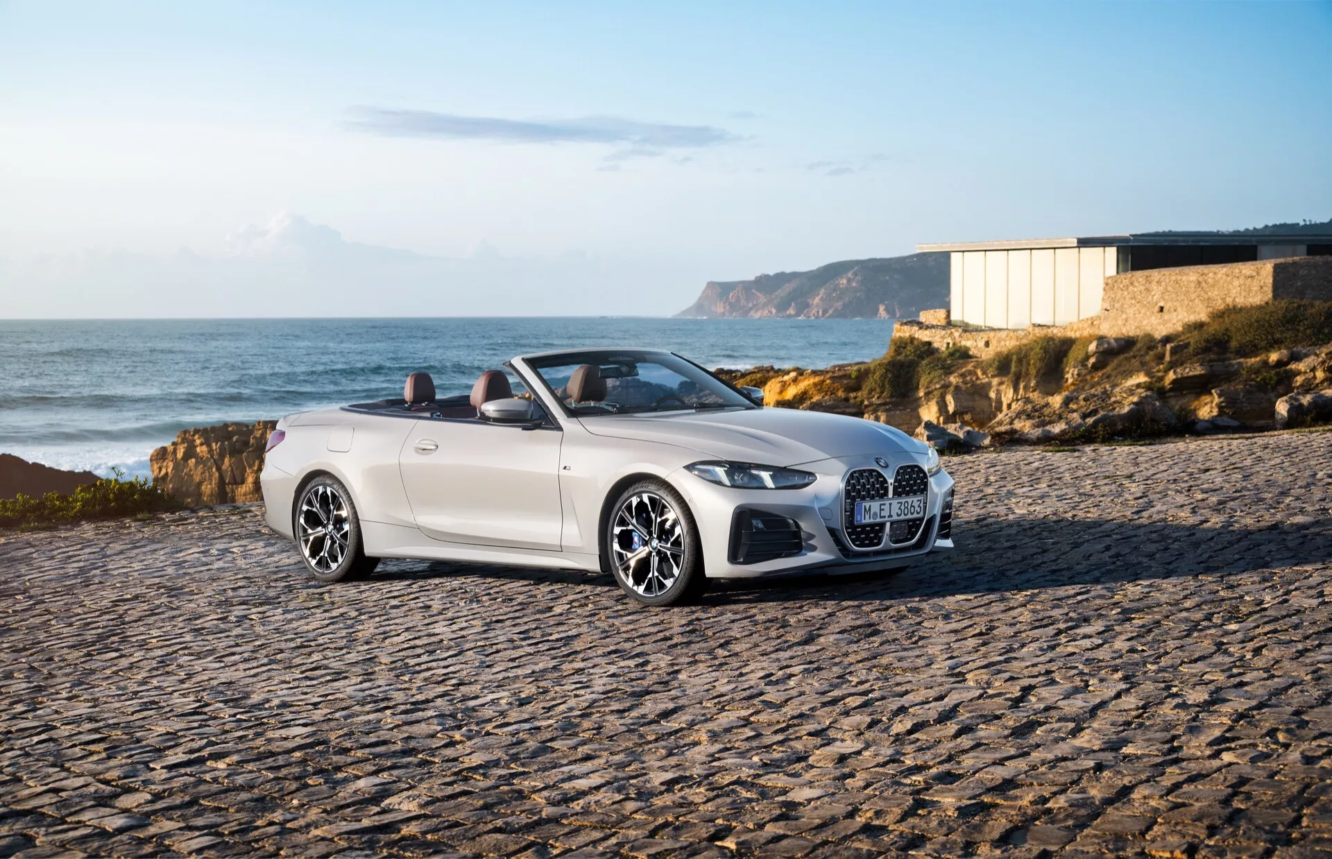 BMW Série 4 Cabriolet (G22-G23-G26-G82-G83 Restylée) 2024 garée sur des pavés dans un environnement côtier, montrant le côté avant-gauche, phares LED, grande grille en maille et jantes élégantes sous la lumière chaude de la fin d'après-midi