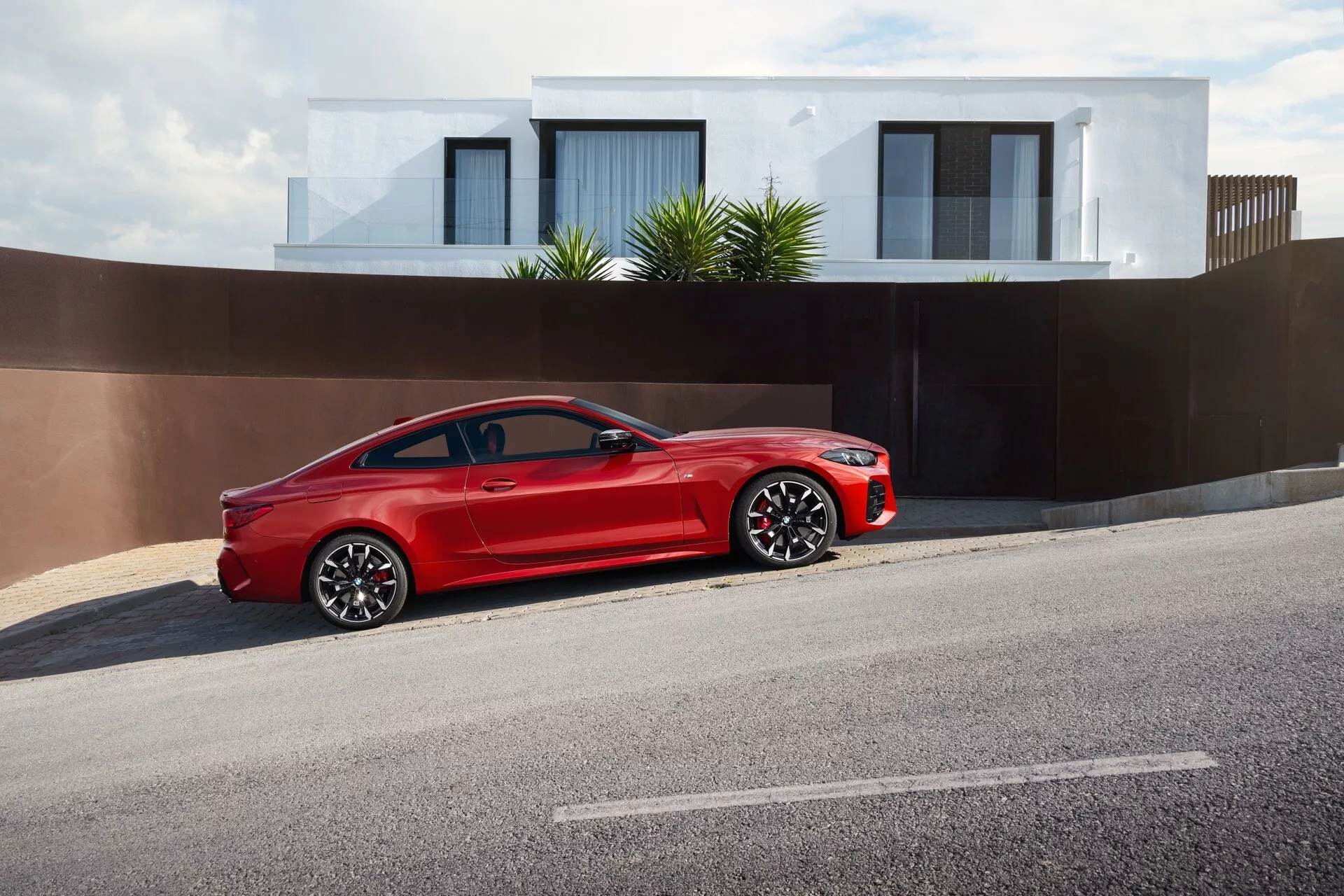 Coupé deux portes rouge vif BMW Série 4 (G22-G23-G26-G82-G83 Facelift) de 2024 garé sur le côté de la rue, montrant son design élégant et sportif avec une grande grille distinctive, des phares LED, des roues en alliage à multiples branches, des pneus à profil bas, une finition de peinture brillante de haute qualité, des miroirs latéraux avec clignotants intégrés et un système de freinage haute performance dans une zone résidentielle.