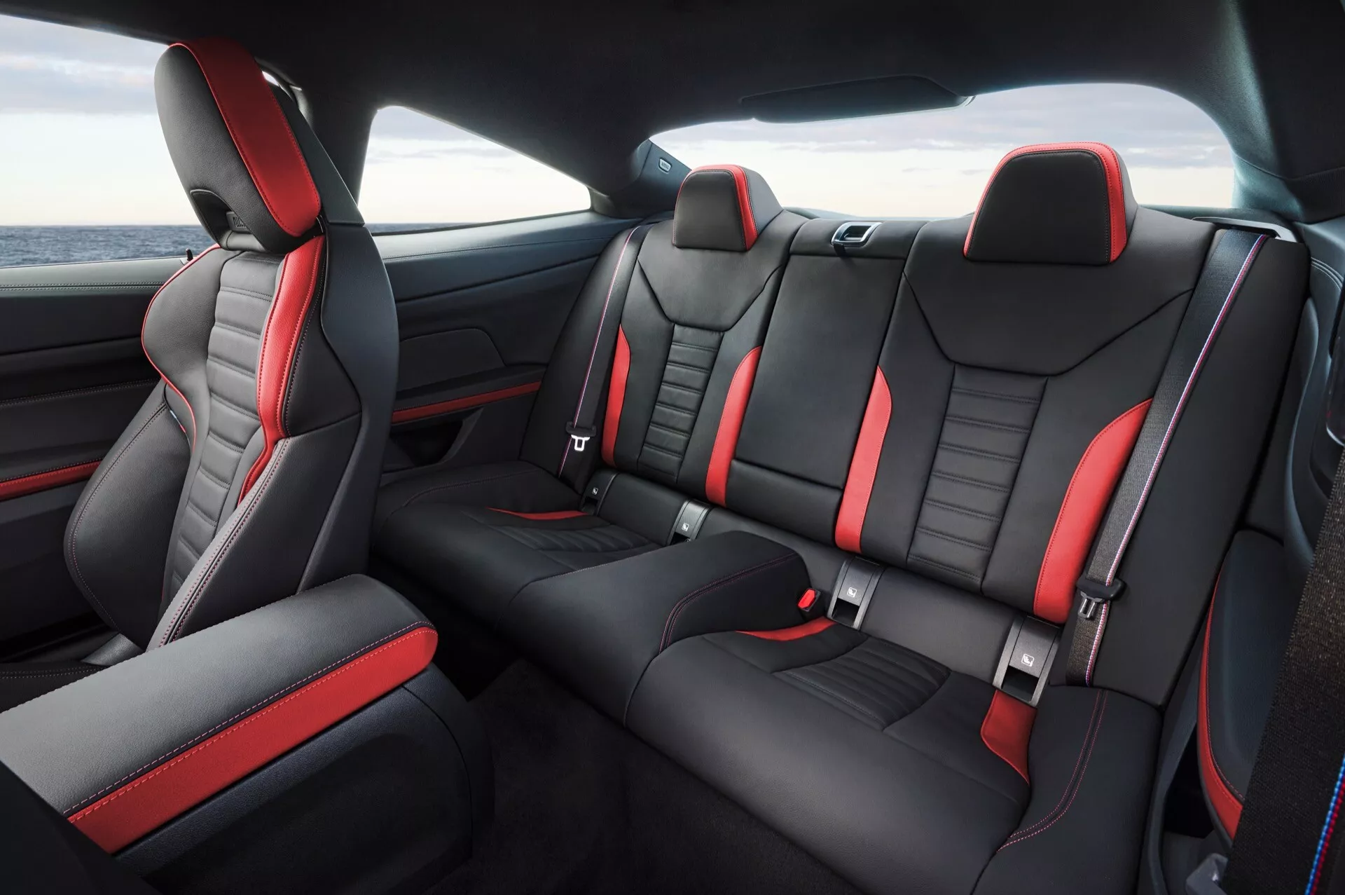 Vue intérieure de la BMW Série 4 2024 (G22-G23-G26-G82-G83 FAL) montrant la zone des sièges arrière avec un design sportif, des sièges en cuir et Alcantara noirs et rouges, et des caractéristiques de sécurité avancées
