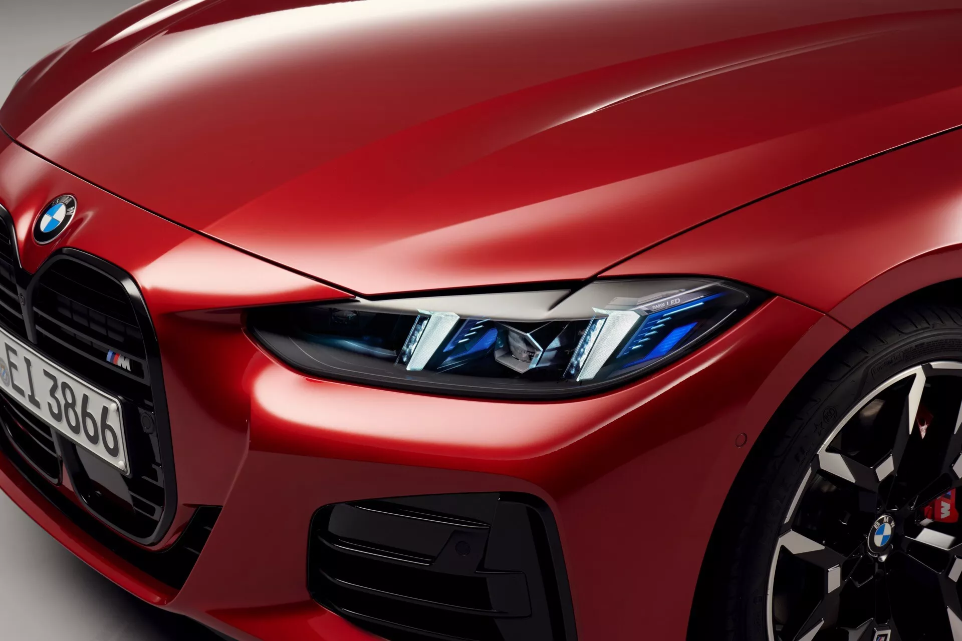 Gros plan d’une BMW Série 4 rouge de 2024 (restylage G22-G23-G26-G82-G83) mettant en avant le quart avant gauche soulignant les phares LED avec yeux d'ange, un aperçu de la calandre iconique en forme de rein, roue en alliage sportive avec frein haute performance, peinture métallisée et carrosserie avec détail de prise d’air, et badge BMW partiel et identificateur de série visible.