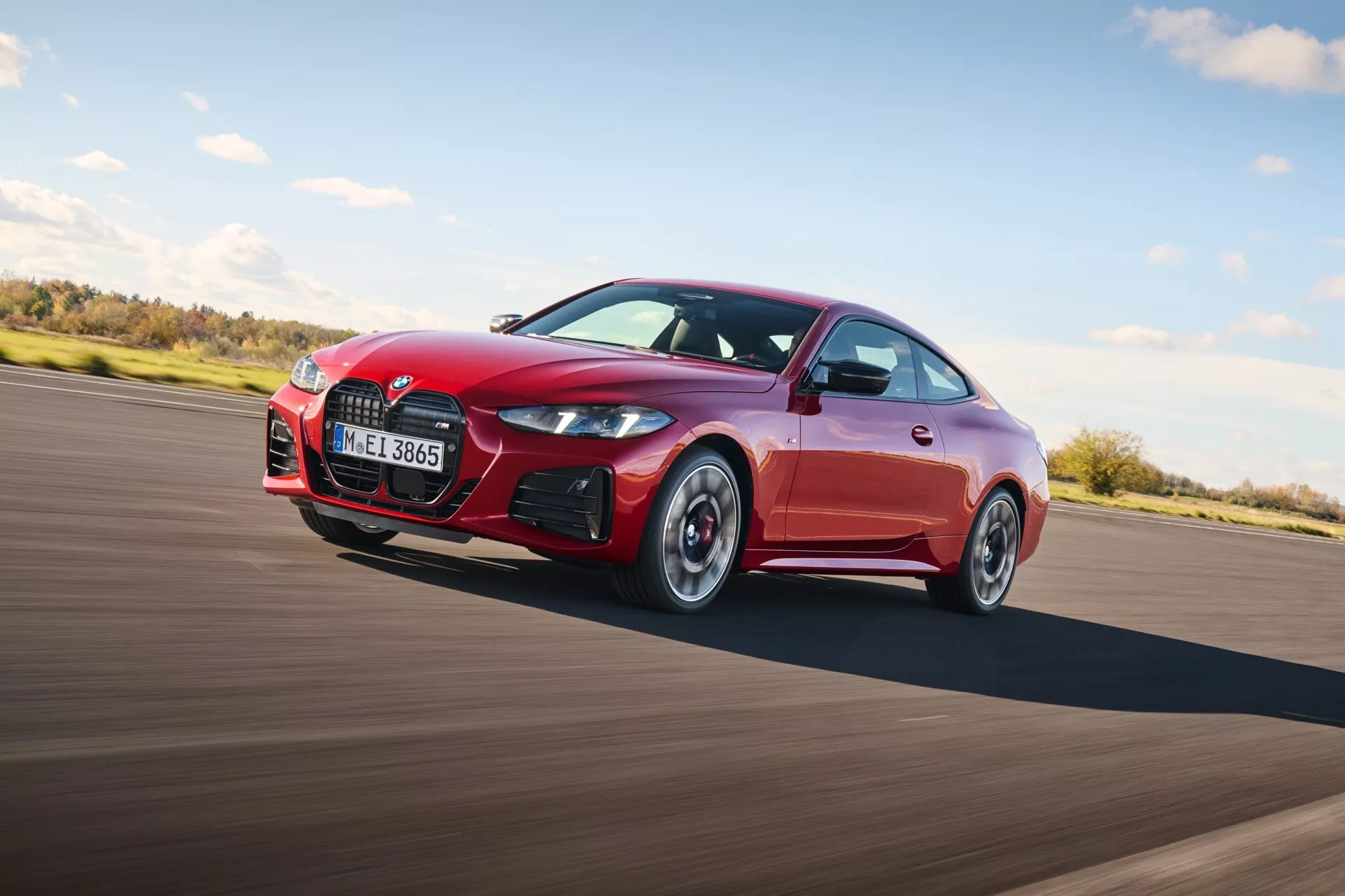 Vue dynamique d'un coupé sportif rouge BMW Série 4 (G22-G23-G26-G82-G83 Facelift) en mouvement mettant en avant un design élégant, une grille frontale distinctive, un pare-choc sportif avec prises d'air et des caractéristiques orientées vers la performance, capturée à un angle de 45 degrés soulignant le profil aérodynamique.