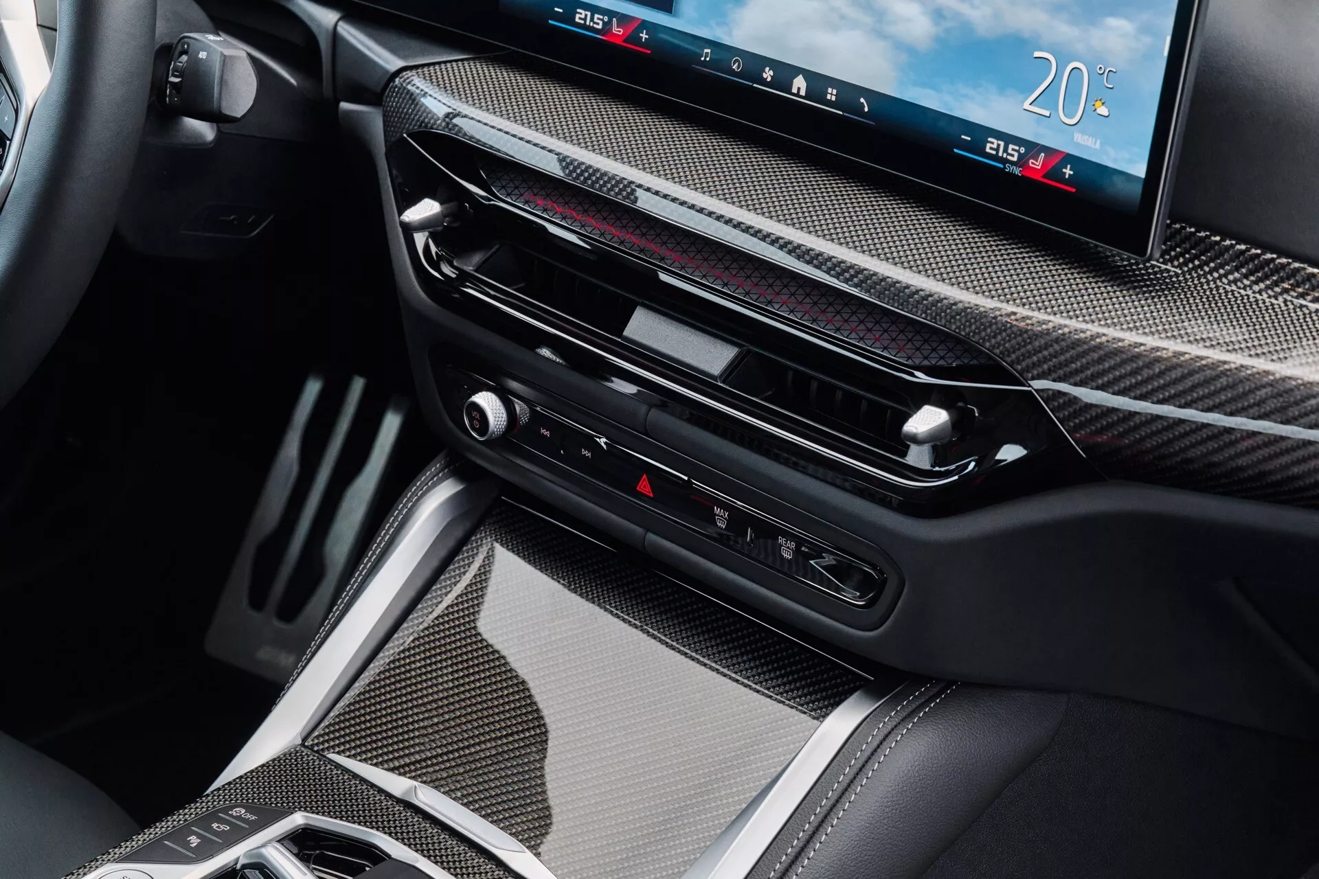 Vue intérieure détaillée de la BMW Série 4 modèle 2024 présentant la zone de la console centrale avec garniture en fibre de carbone, un grand écran numérique pour le système d'infodivertissement et le contrôle du climat, des bouches d'air fines, des boutons tactiles incluant le contrôle des feux de détresse, et un levier de vitesse électronique moderne, symbolisant la technologie de transmission avancée et le luxe.