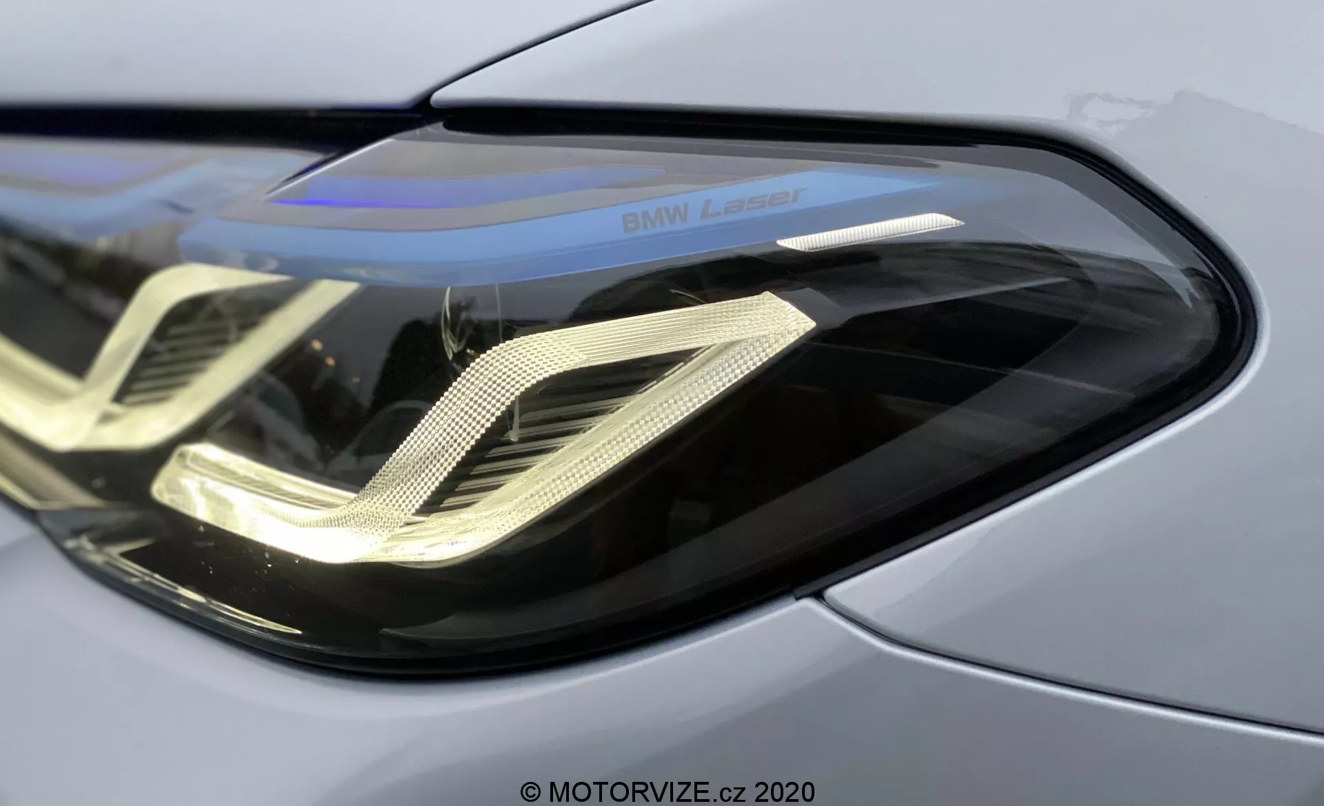 Gros plan sur le phare avant gauche de la BMW 520i Touring Steptronic 2020, présentant une coque en polycarbonate incurvée et élégante, des feux diurnes à LED en forme de double hélice, un boîtier réfléchissant et le marquage 'BMW Laser', soulignant la technologie avancée des phares laser et le panneau de carrosserie métallique premium.