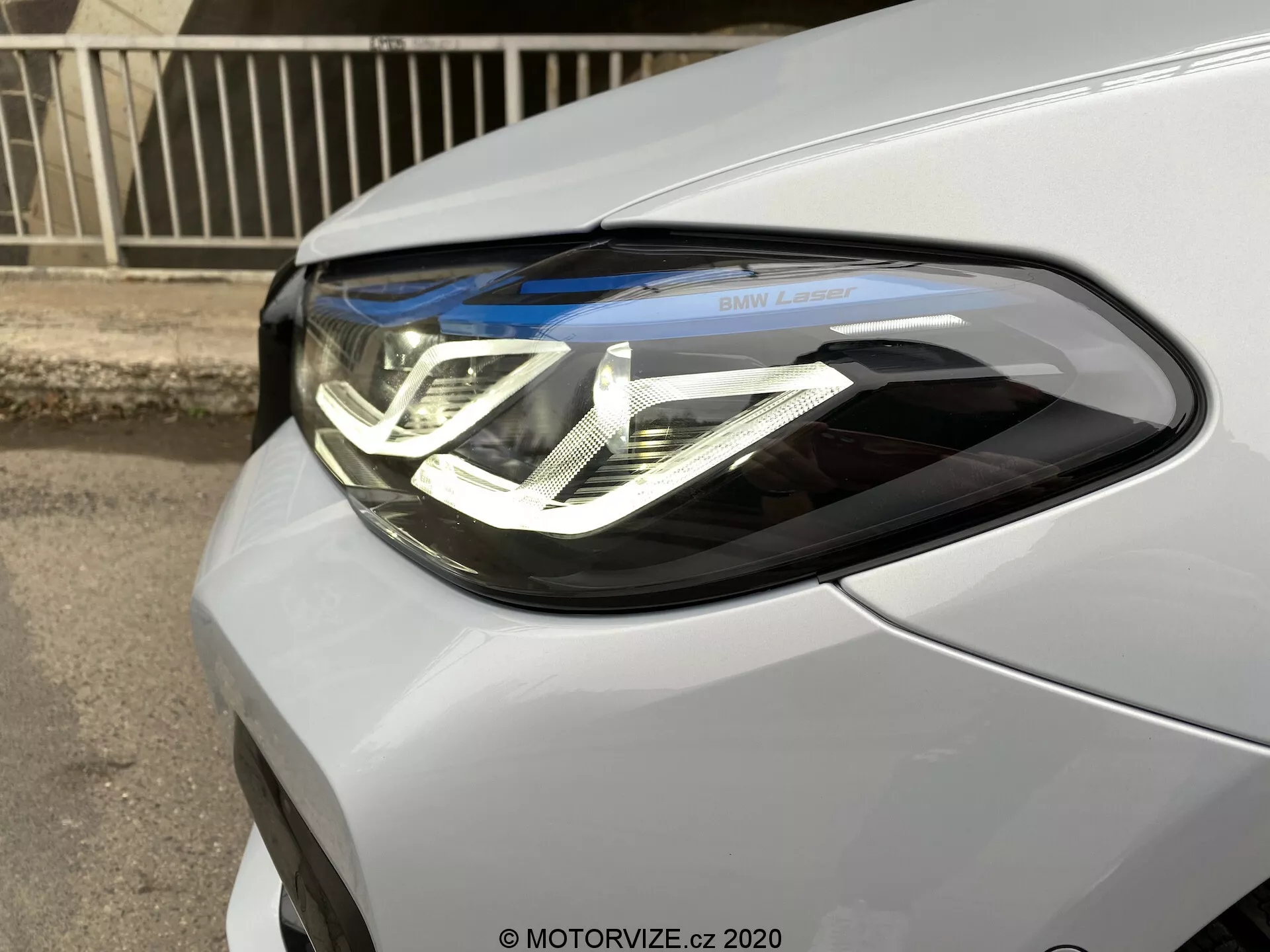 Gros plan sur le phare côté conducteur de la BMW Série 5 2020 (BMW 520i Touring Steptronic). L'image capture la voiture sous un angle avant trois quarts, mettant en valeur les feux de jour à LED avec un design en double U, les lentilles du projecteur et l'inscription 'BMW Laser'. L'unité de phare s'intègre parfaitement dans la finition métallique ou nacrée de la voiture.