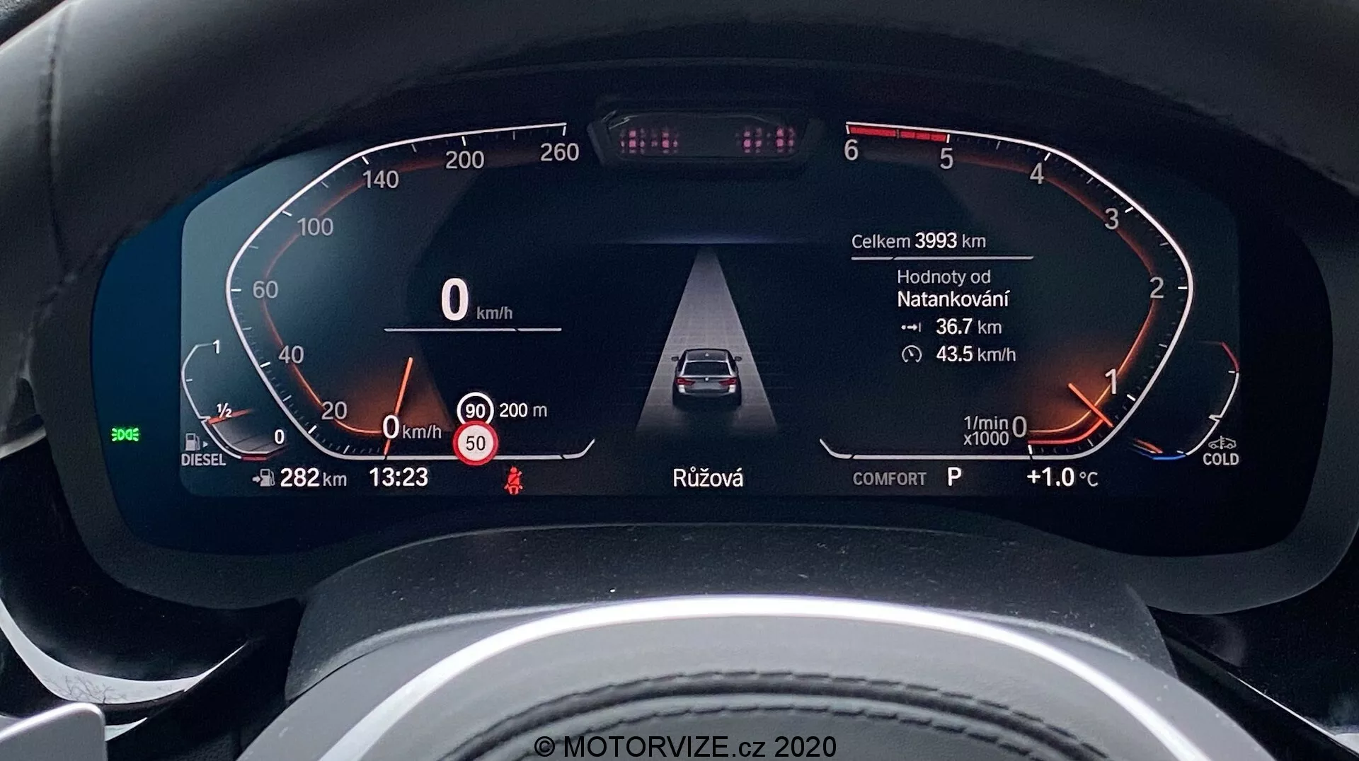 Vue rapprochée du tableau de bord numérique d'une BMW Série 5 2020 (BMW 520i Touring Steptronic) prise du point de vue du conducteur. Le tableau de bord numérique affiche des informations clés telles que la vitesse du véhicule (0 km/h), une jauge de carburant marquée pour le diesel, des avertissements de porte ouverte et de ceinture de sécurité, des systèmes avancés d'assistance à la conduite comme le régulateur de vitesse adaptatif, un compte-tours au ralenti avec un indicateur de moteur froid, et des données supplémentaires telles que le kilométrage (39933 km), la température extérieure (+1.0°C), l'heure (13:23), la sélection de la vitesse (P pour stationnement) et le mode de conduite (confort). Le design est élégant et moderne, indiquant un véhicule haut de gamme.