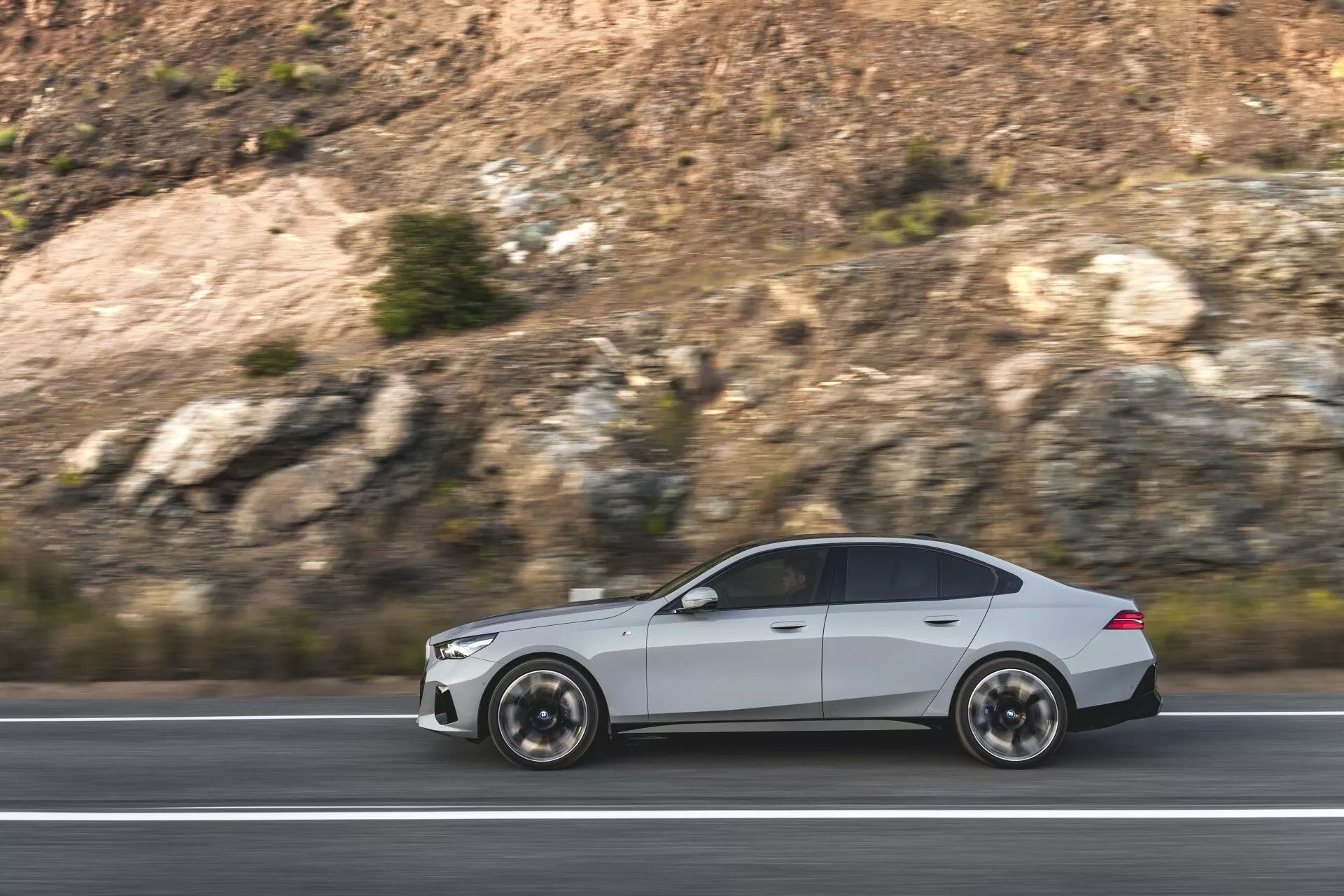 BMW Série 5 (G60-G61) de 2023 en mouvement, présentant son design aérodynamique et son esthétique sportive avec des roues à multiples branches visibles et des contours de carrosserie élégants, capturée de côté dans un cadre autoroutier