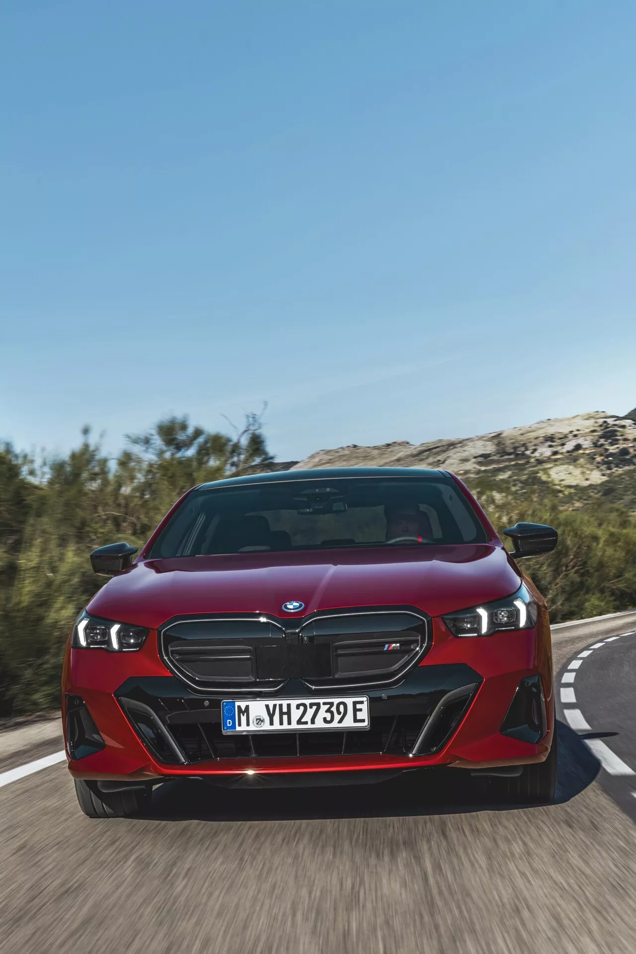 BMW Série 5 (G60-G61) 2023 en rouge, présentant sa grille à double rein distinctive, phares LED et façade avant dynamique sous un angle bas de face sur une route, soulignant la vitesse du véhicule et les fonctionnalités électrifiées avancées iPerformance
