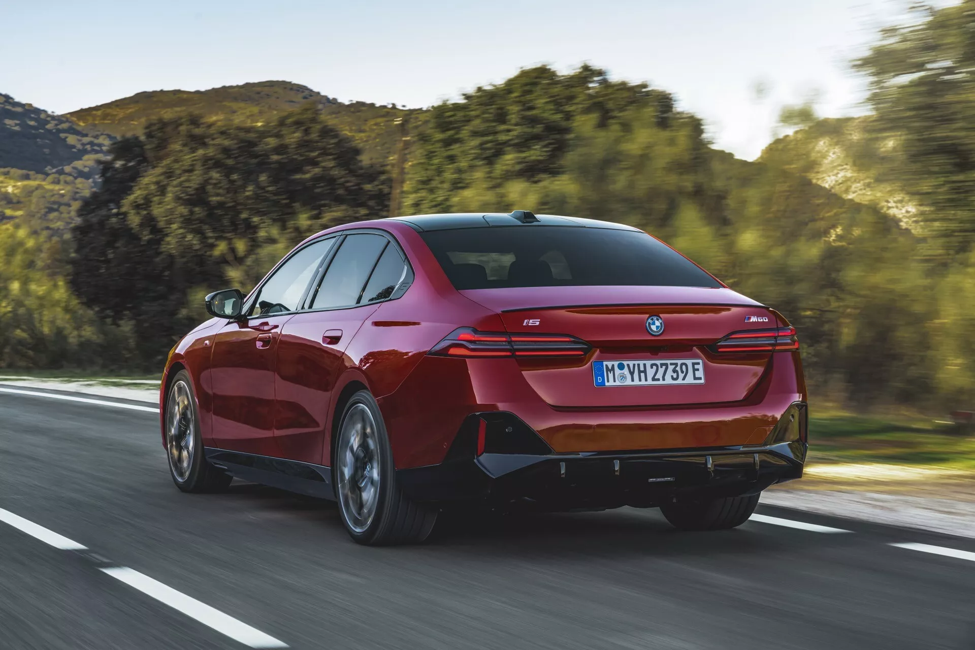 Sedan moderne BMW Série 5 (G60-G61) de 2023 roulant sur une route ouverte, offrant une vue arrière aux trois quarts montrant les feux arrière élégants, le pare-chocs arrière sportif avec sorties d'échappement intégrées, et une silhouette distinctement coupé.