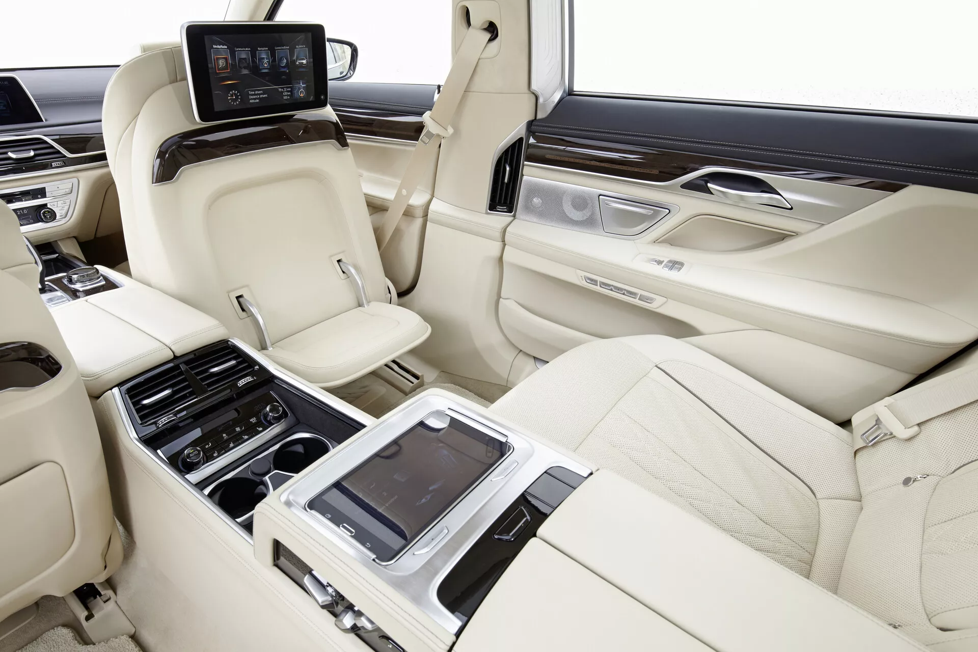 Image de l'intérieur de la cabine arrière de la BMW 7er-reihe (G11-G12) de 2015, capturant l'espace et le luxe des sièges vus d'une perspective droite. Les sièges en cuir de couleur claire en configuration 2+1, avec un design profilé pour le confort et le soutien, les appuie-têtes et les capacités de réglage individuelles sont visibles. Une console centrale avec divers contrôles et peut-être une interface tactile pour le réglage des sièges, le contrôle de la climatisation et les multimédias est mise en évidence. Les panneaux de porte incluent des garnitures en bois et des accents métalliques brossés avec des contrôles supplémentaires. Des écrans individuels sont montés à l'arrière des sièges avant pour le divertissement et un panneau de contrôle arrière avec un écran est situé derrière la console centrale. L'intérieur du véhicule présente un réglage avancé des sièges, un contrôle de la climatisation et des systèmes de divertissement au sein de finitions de cuir, bois et métal de haute qualité.