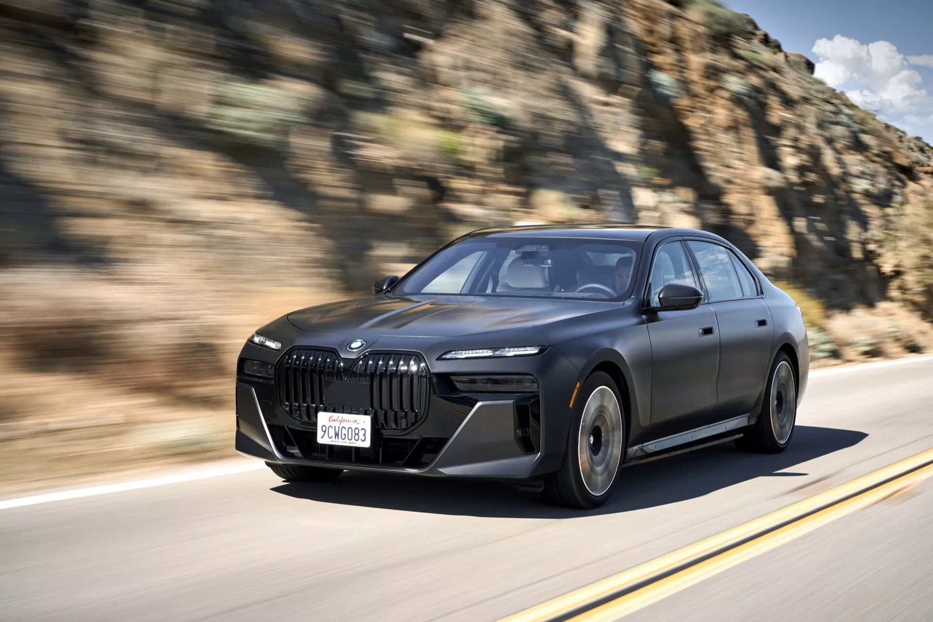 Sedan BMW i7 (G70) quatre portes de 2022 en mouvement, mettant en vedette son design dynamique avec un focus sur la grille avant avancée, les phares LED, les contours aérodynamiques et les jantes en alliage sportives, devant une formation rocheuse naturelle