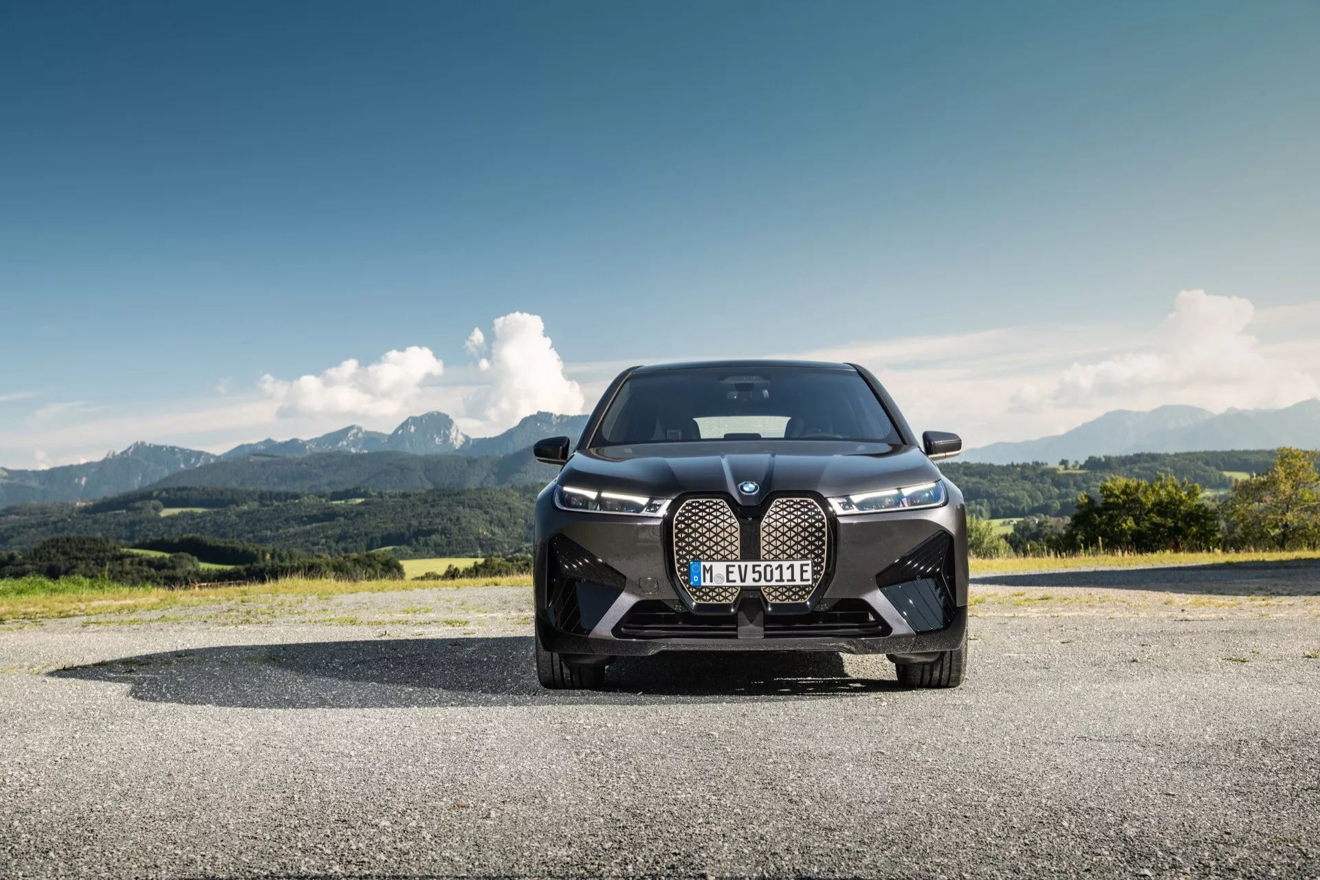 BMW iX (i20) 2021 photographiée depuis un angle avant bas, mettant en avant son design dominant avec une grande calandre en forme de rein, des phares LED élégants et des prises d'air orientées vers la performance devant un paysage montagneux