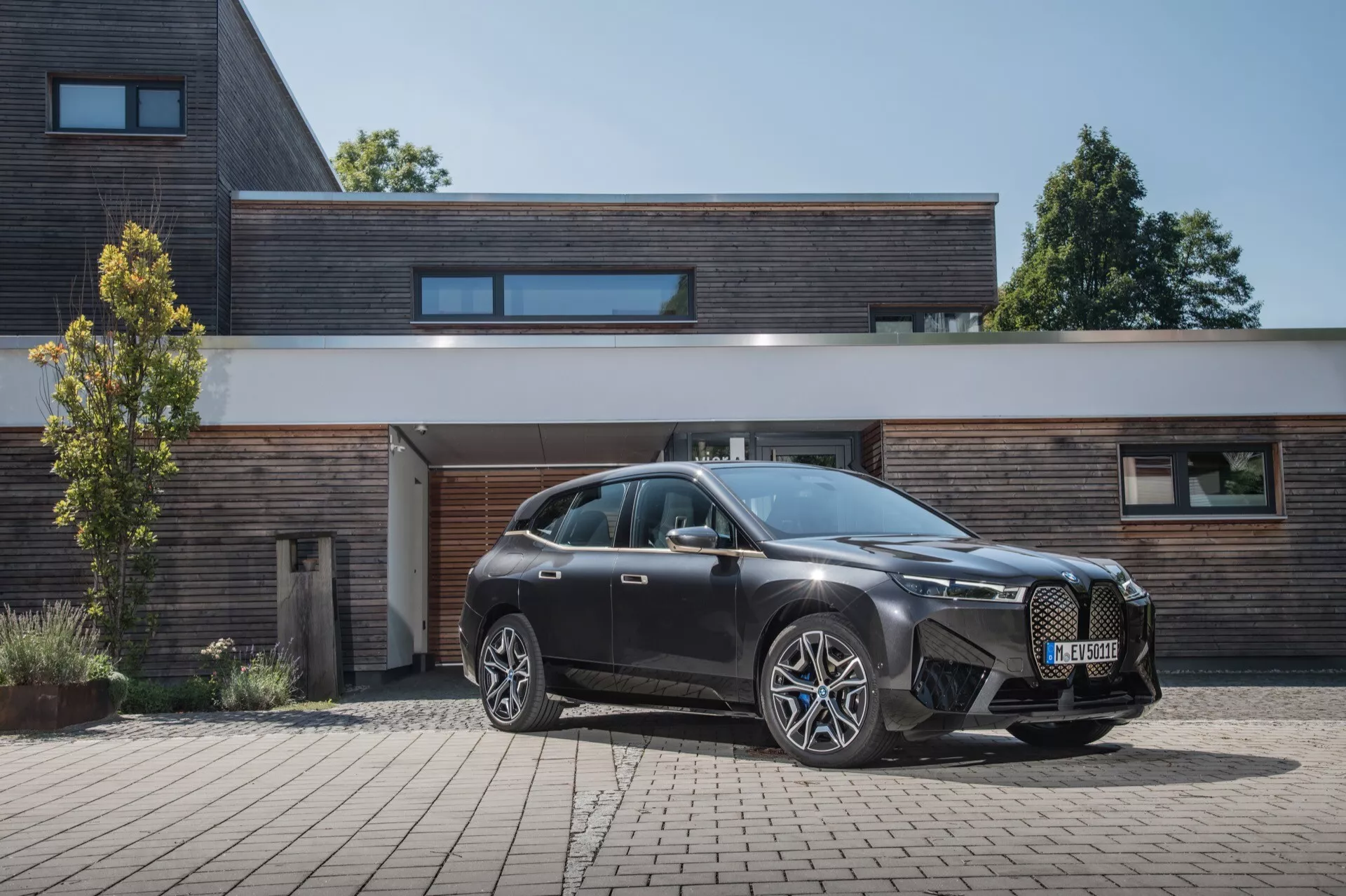 BMW iX 2021 (i20) garée sur une allée montrant sa perspective avant de trois quarts avec un bâtiment résidentiel en arrière-plan, mettant en vedette une grille avant agressive, des phares LED élégants et de grandes roues en alliage à plusieurs branches.