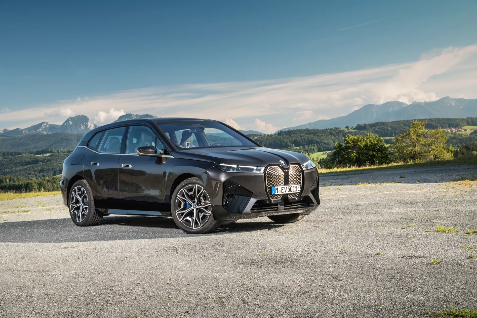 Hatchback moderne à quatre portes BMW iX (i20) de 2021 stationné sur une zone pavée avec un paysage montagneux en arrière-plan, présentant sa grande grille en forme de rein, des lignes épurées, des phares LED et un design aérodynamique avec de grandes roues en alliage