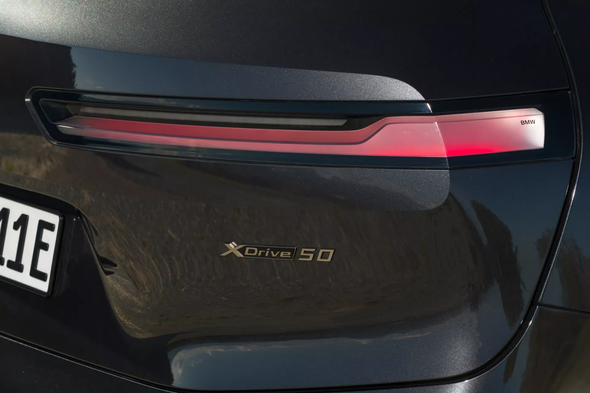 Gros plan sur la section arrière de la BMW iX 2021 (i20) mettant en lumière le feu arrière LED, le badge xDrive 50 et la finition haute brillance