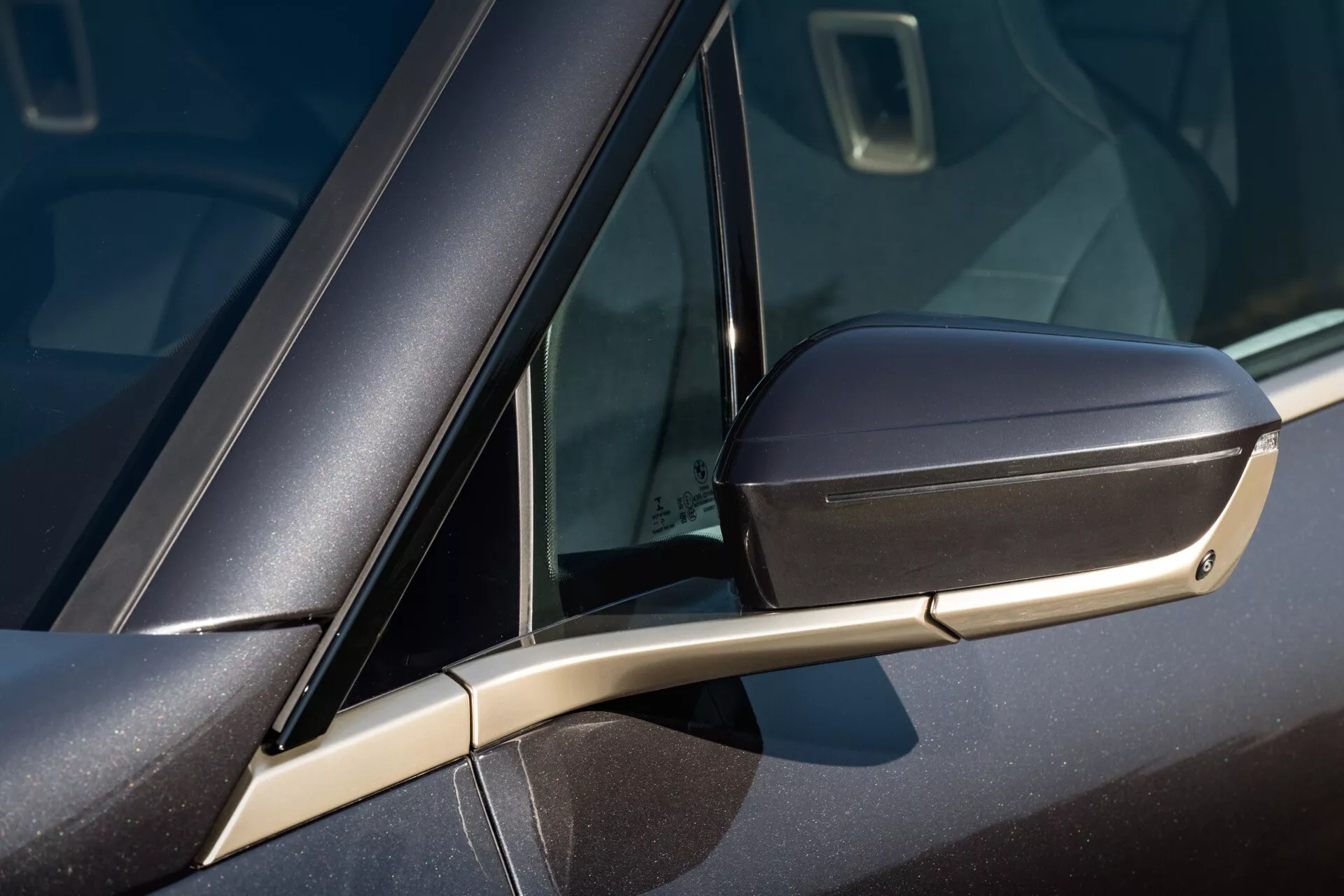 Vue rapprochée d'une BMW iX 2021 (i20) montrant le design détaillé du rétroviseur latéral assorti à la couleur avec clignotant intégré, le pont de support aérodynamique élégant et une partie de la fenêtre avec petit vitrage.