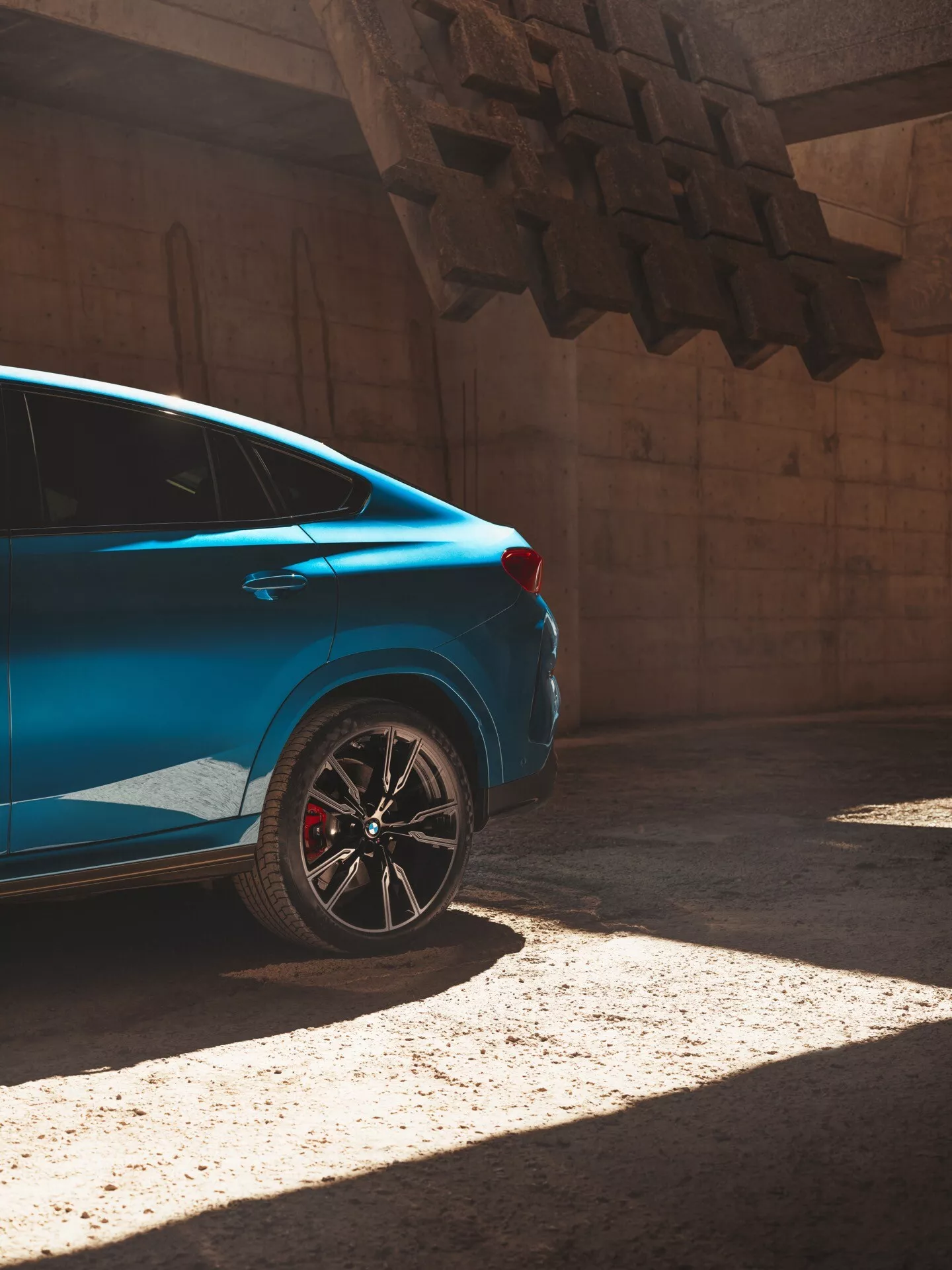 Voiture bleue BMW X6 2023 (G06/F96 facelift) sous le soleil, vue depuis une perspective arrière de trois quarts mettant en évidence le quart arrière avec jante sportive et étrier de frein rouge.