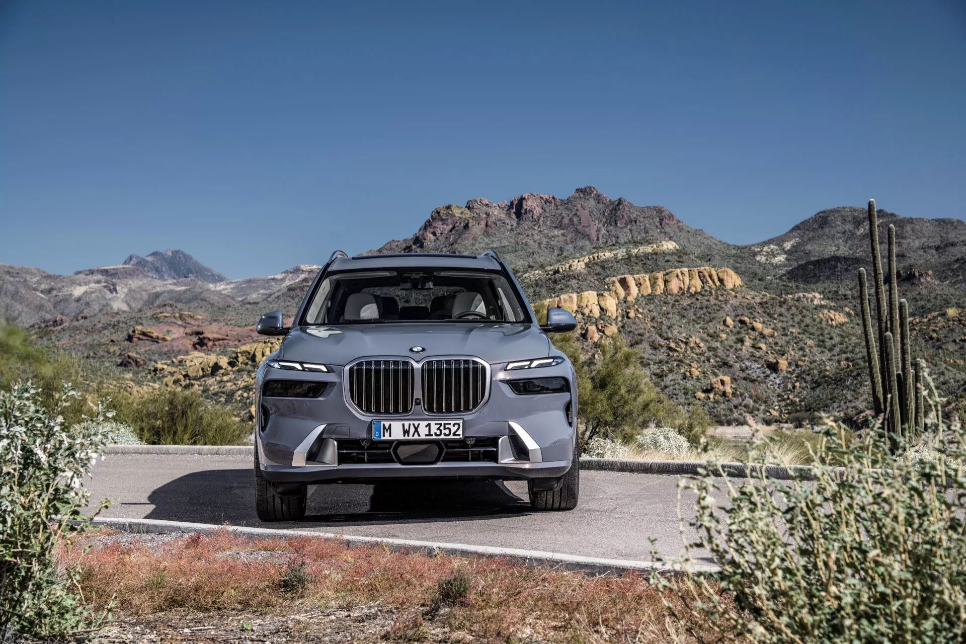 SUV de luxe BMW X7 2022 (G07-Facelift), présentant un design moderne avec une grande calandre en forme de rein, des phares LED élancés, un pare-choc avant avancé avec des fonctions ADAS, un capot sculpté et des roues en alliage, garé de manière proéminente sur une route contre un fond de montagnes désertiques sous un ciel bleu clair