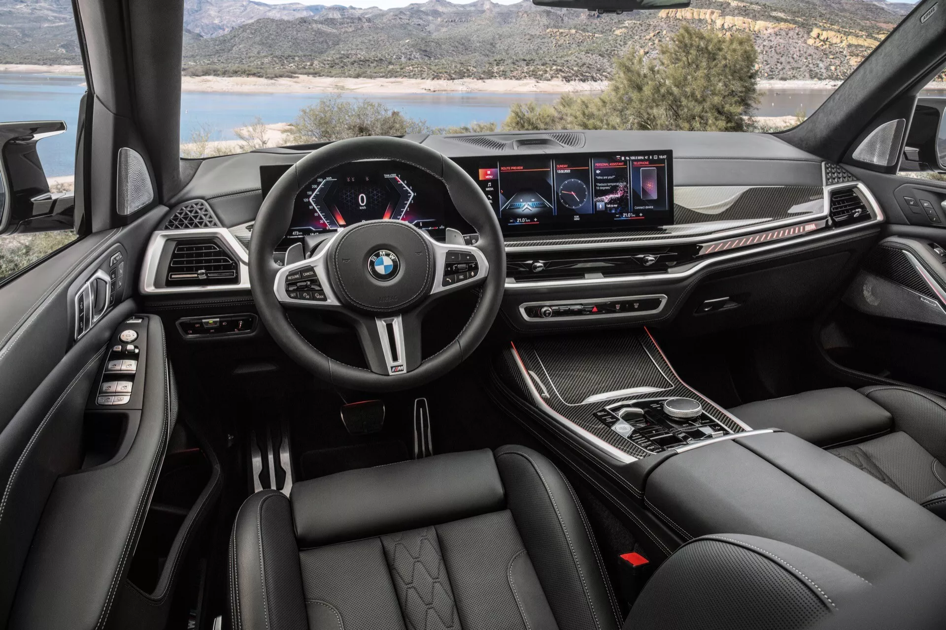 Vue intérieure du BMW X7 2022 (G07 Restylage) depuis la perspective du conducteur avec volant multifonction avec logo BMW, tableau de bord numérique, écran d'infodivertissement large, boutons de contrôle de climatisation, sélecteur de vitesse automatique, matériaux luxueux, sièges sportifs et confortables, et éclairage d'ambiance