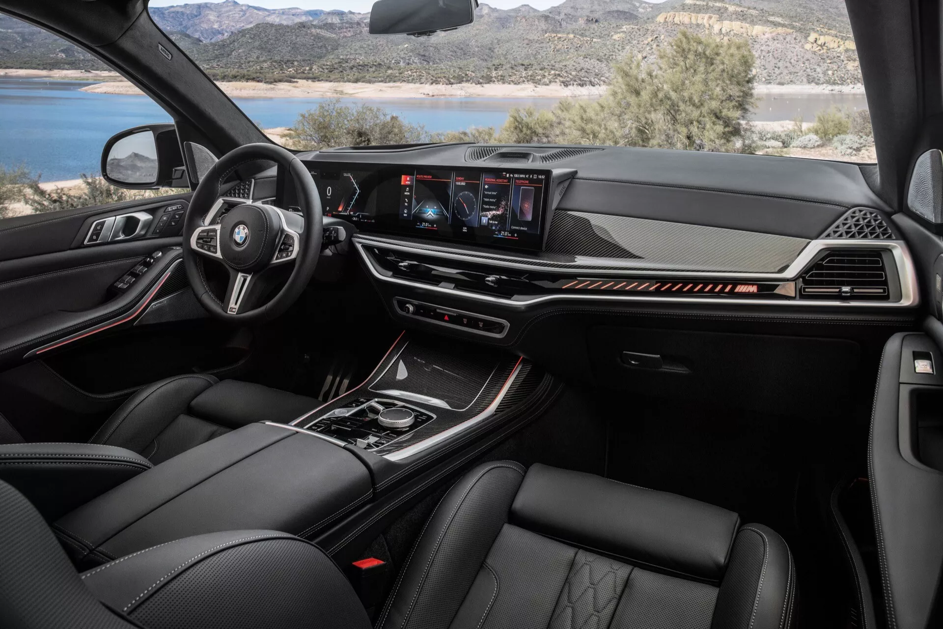 Intérieur du BMW X7 (G07-facelift) 2022 présentant le volant multifonction en cuir avec logo du fabricant, tableau de bord numérique, système d'infodivertissement central tactile, et matériaux haut de gamme incluant des sièges en cuir avec des fonctionnalités de contrôle climatique avancées depuis la perspective du passager avant