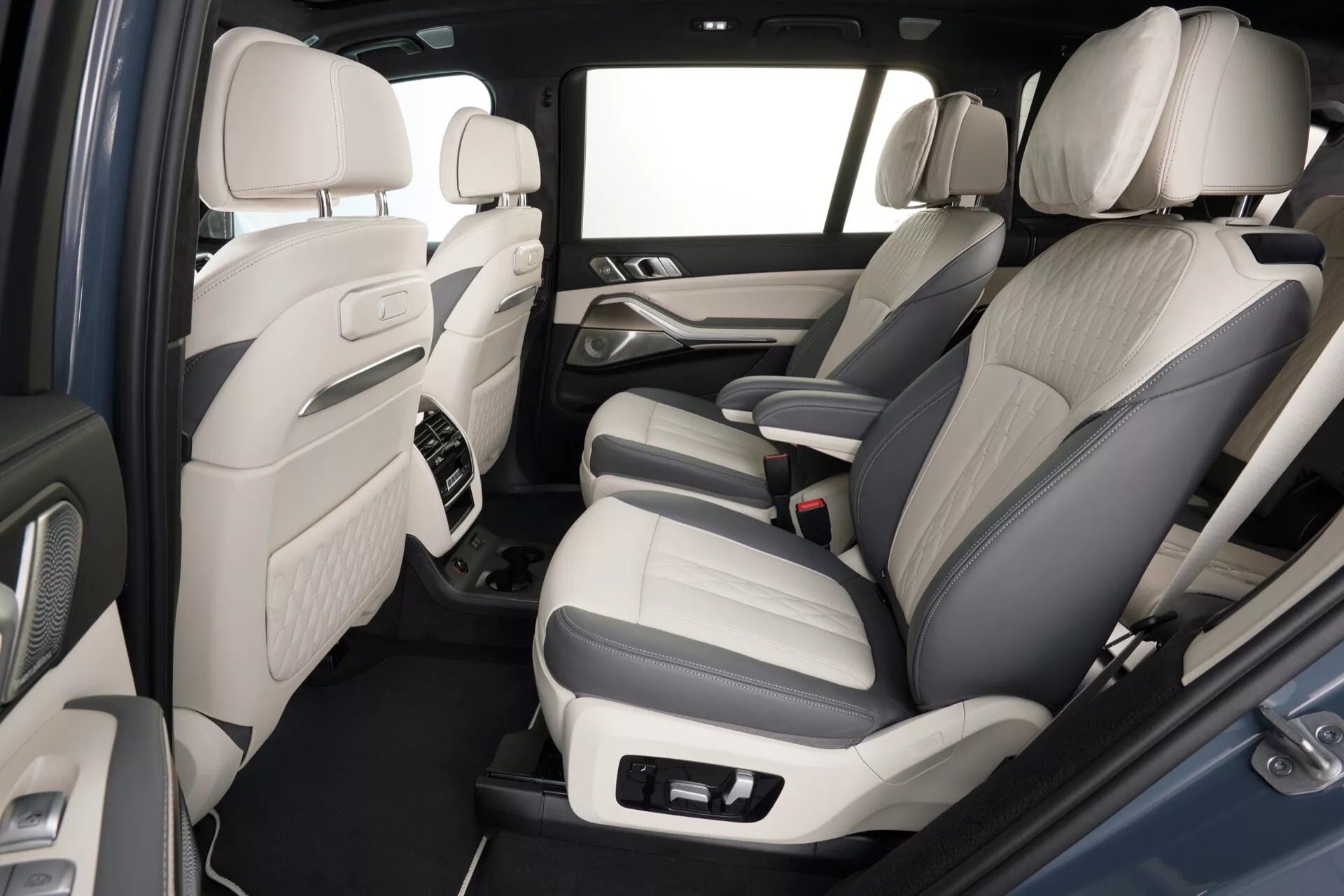 Vue intérieure du BMW X7 (G07 Facelift) 2022 mettant en valeur le compartiment passagers arrière, avec une sellerie en cuir bicolore, des commandes de système audio avancé sur les panneaux de porte, console centrale avec des accents de matériaux de haute qualité, sol tapissé, espace généreux pour les jambes et un schéma de couleur intérieur clair pour une sensation d'espace dans la cabine