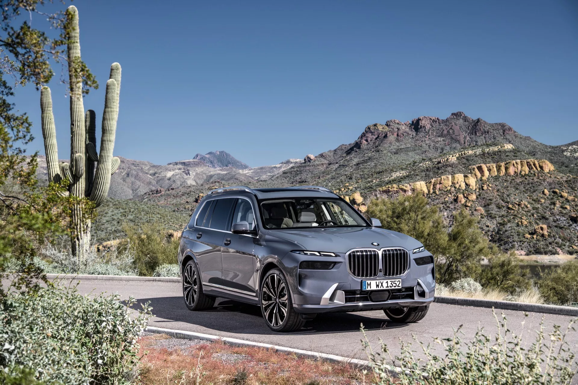 Vue avant trois quarts du BMW X7 2022 (G07-Facelift) sur une route pavée, montrant sa grille frontale expansive en forme de rein, phares LED angulaires, capot sculpté et profil côté conducteur contre un fond désertique et montagneux en plein jour.