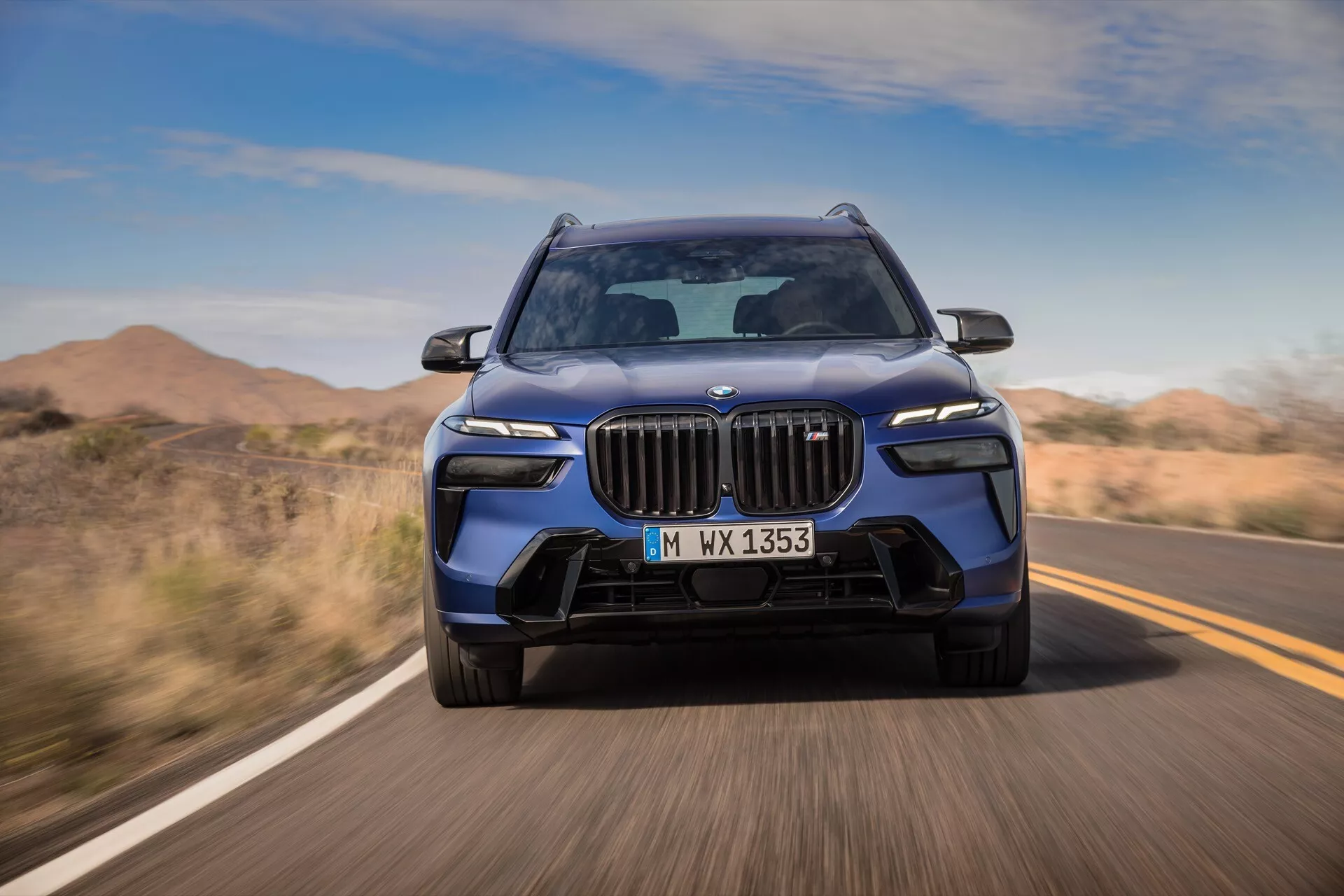 BMW X7 2022 (G07-Facelift) en mouvement, perspective avant dynamique mettant en avant la calandre, les phares LED et le pare-chocs sportif sous un ciel dégagé sur une route désertique