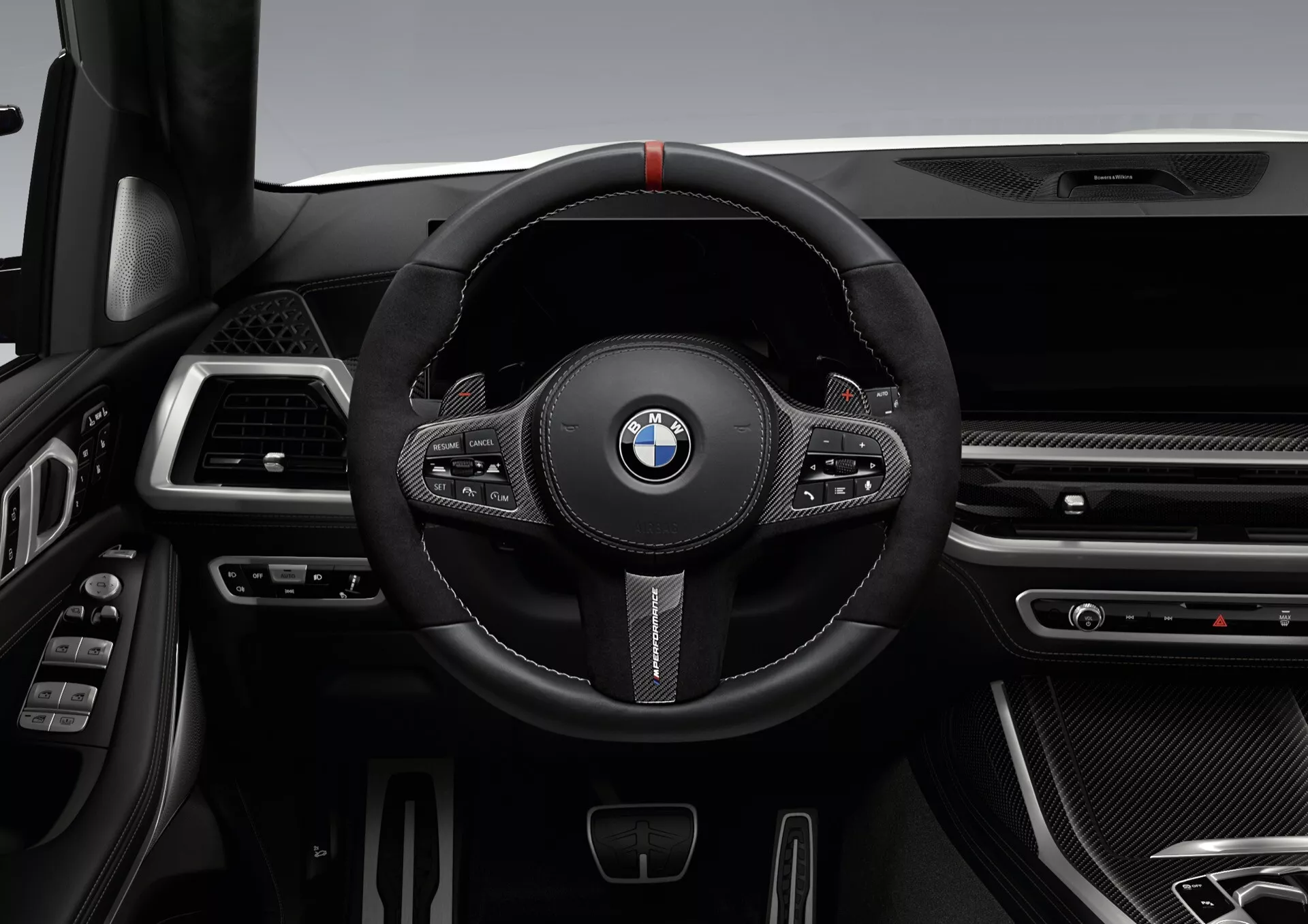 Intérieur du BMW X7 2022 (G07-Facelift) mettant en avant le volant sportif en cuir noir marqué d'un repère rouge, boutons multifonctions et palettes de changement de vitesse, face à un tableau de bord sophistiqué avec élégantes aérations, textures façon fibre de carbone et finitions chromées