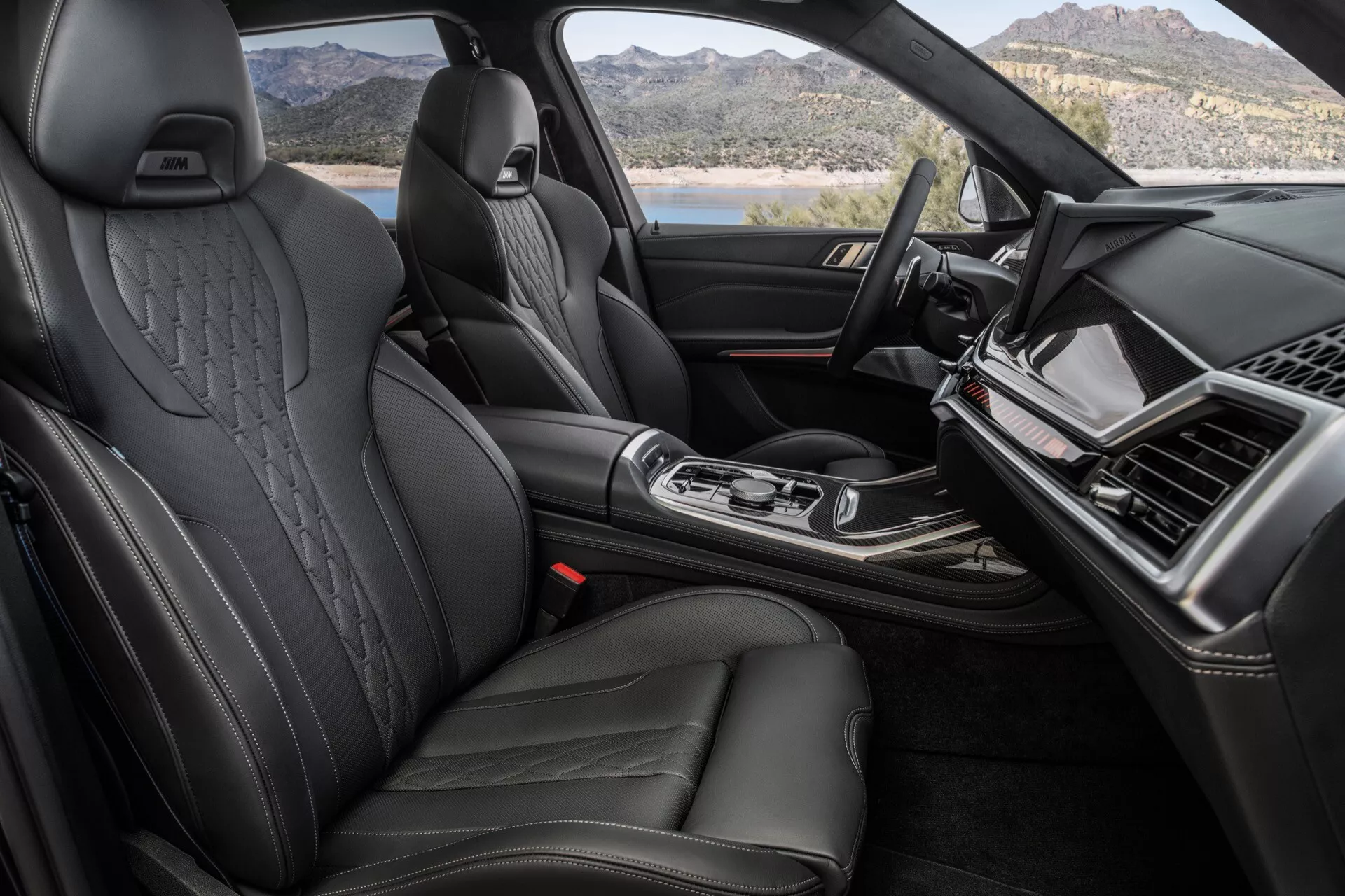 Vue intérieure du BMW X7 2022 (G07-Facelift) centrée sur l'habitacle avant premium avec sièges en cuir noir dotés de renforts latéraux et de repose-têtes en relief, tableau de bord élégant avec écran d'infodivertissement, console centrale avec levier de vitesse ergonomique, et finitions haut de gamme indiquant un véhicule de luxe.