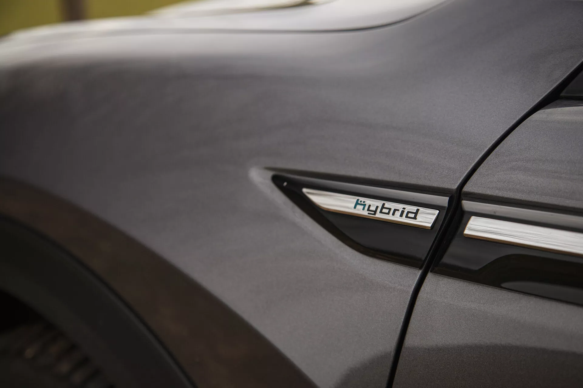 Détail en gros plan du Citroën C5-X 2022 montrant l'insigne Hybride sur le profil latéral inférieur près du passage de roue arrière, mettant en avant la technologie hybride et l'esthétique du design sous des conditions d'éclairage doux