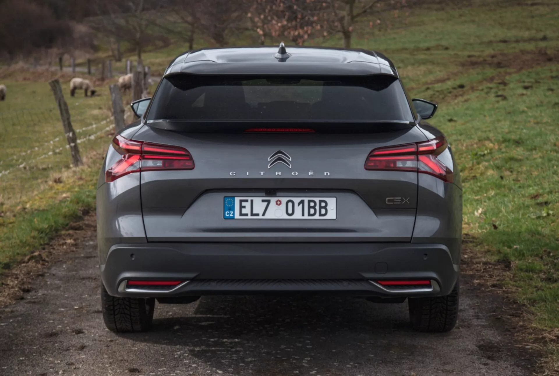 Vue arrière du Citroën C5X 2022 sur un chemin de gravier avec un arrière-plan naturel, mettant en avant des feux arrière LED, le contrôle de distance au stationnement, un double échappement et d'autres détails extérieurs.