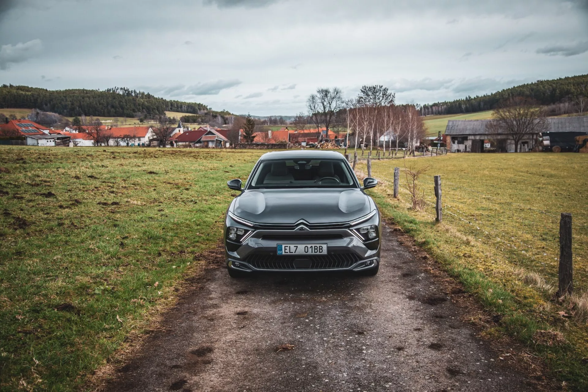 Vue frontale d'une Citroën C5-X 2022 sur un chemin étroit dans un champ herbeux sous un ciel couvert, mettant en avant son design élégant, sa grille complexe avec emblème, ses unités de phares LED angulaires, les lignes sculptées du capot et les éléments supplémentaires d'éclairage avant, immatriculée en République tchèque.