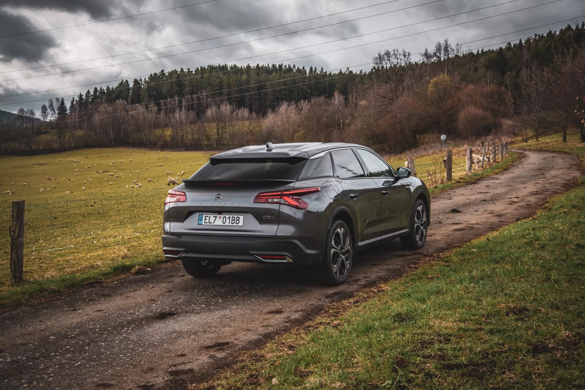 Citroen C5-X 2022, hatchback moderne garée sur un chemin rural non pavé, vue arrière trois quarts mettant en évidence un design aérodynamique avec spoiler et antenne aileron de requin, feux arrière minces et horizontaux et roues larges à multiples branches, suggérant des performances et un luxe en milieu non urbain.