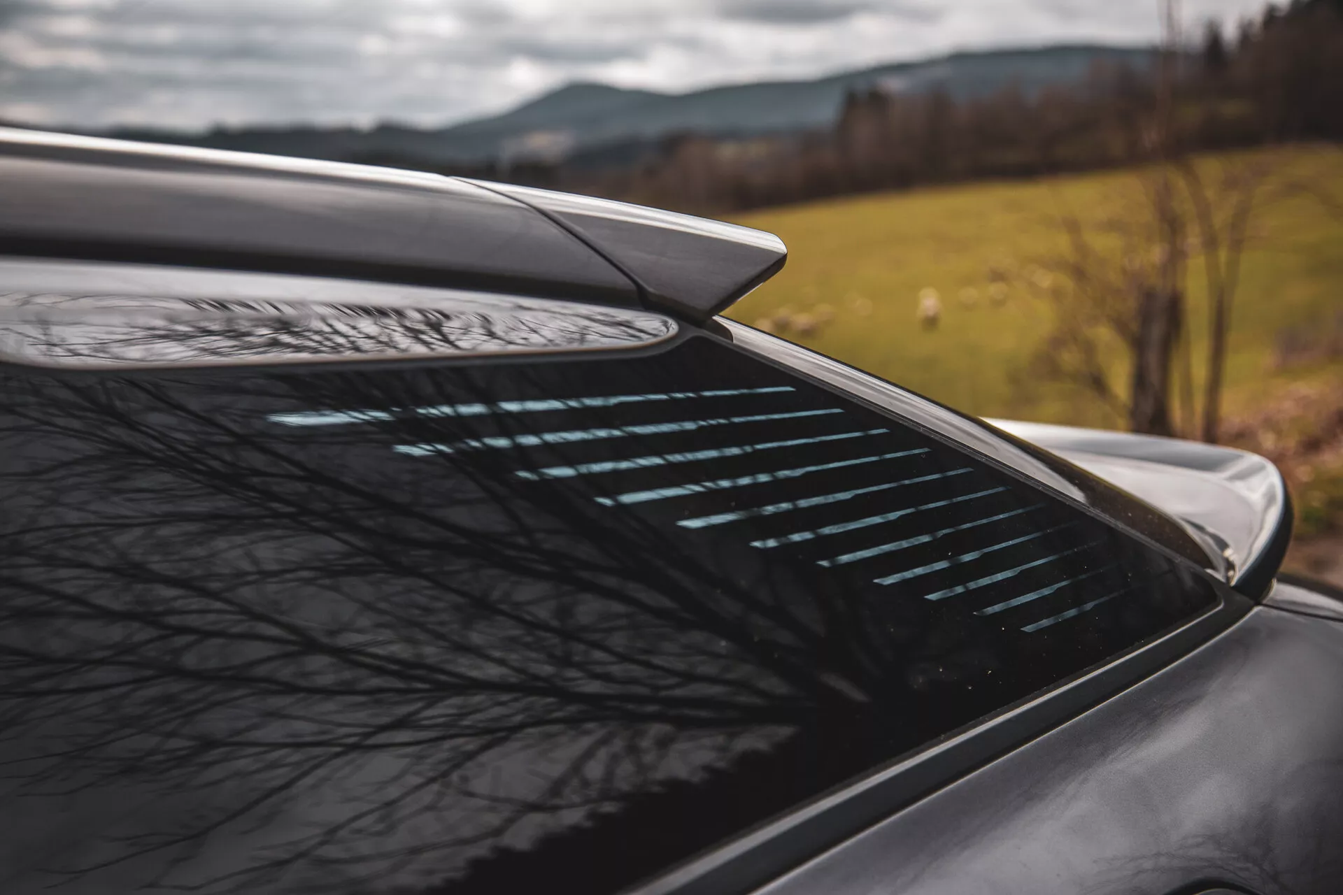 Vue de côté en gros plan de la section arrière de la Citroen C5-X 2022 avec spoiler aérodynamique intégré et lunette arrière dégivrante sur fond naturel flou, suggérant des caractéristiques de performance et de sécurité du véhicule dans un cadre potentiellement rural