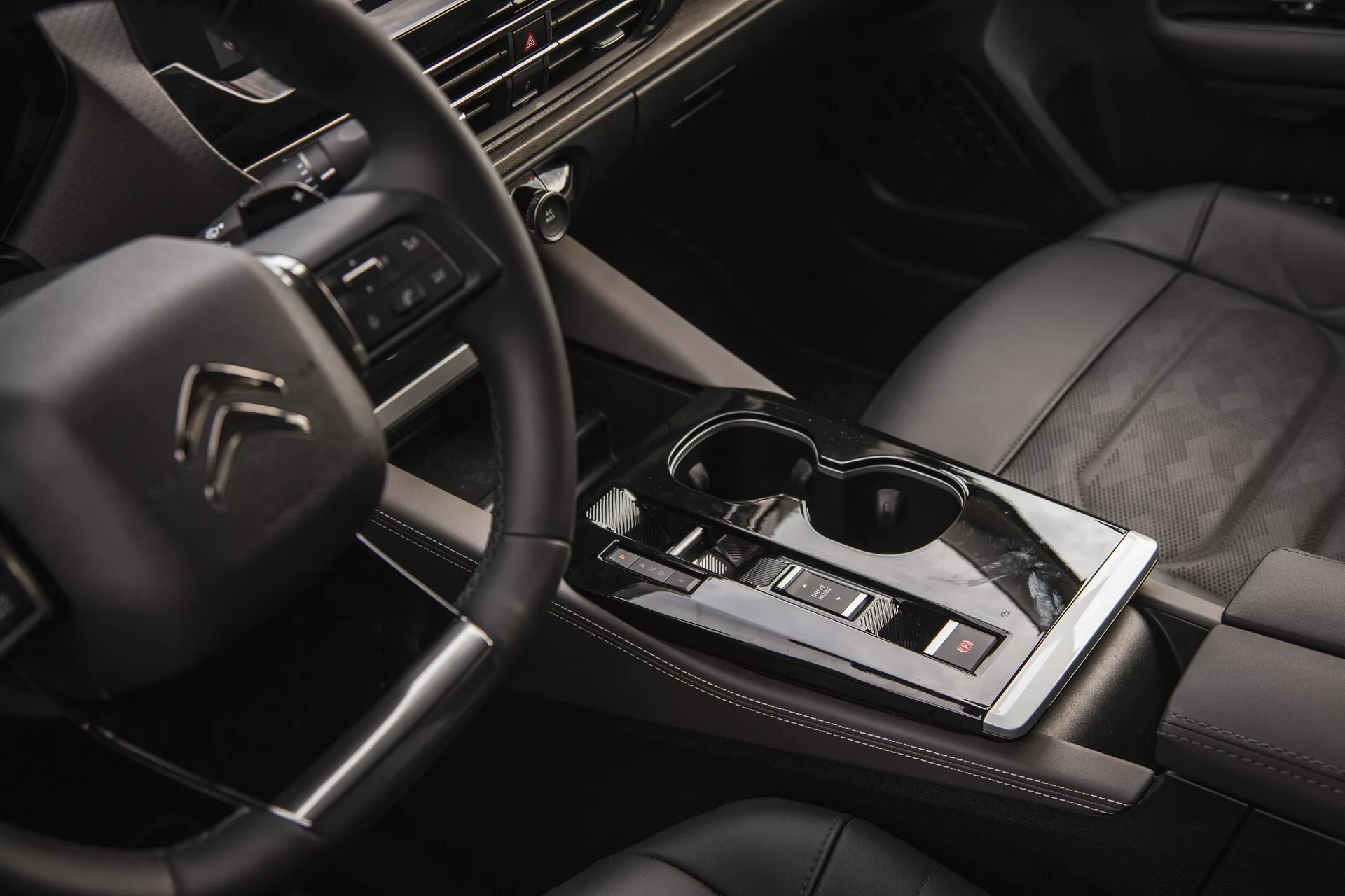 Vue intérieure de la Citroën C5-X 2022 montrant le volant multifonction avec logo, tableau de bord haute technologie avec système d'infodivertissement, levier de vitesse automatique élégant, contrôle climatique, sièges en cuir avec coutures de qualité et une touche de style de vie avec des lunettes de soleil sur la surface centrale brillante