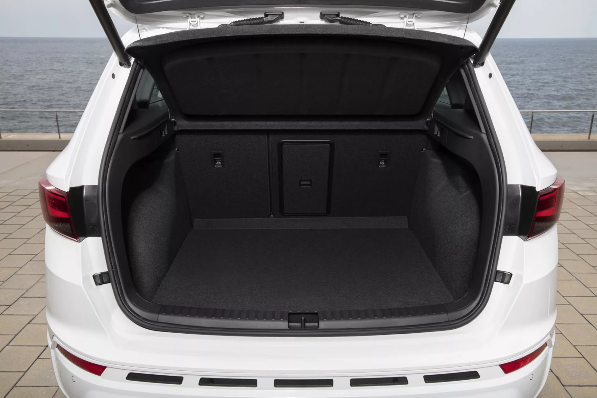 Vue arrière du SUV blanc Cupra Ateca 2020 avec le coffre ouvert montrant un espace de chargement spacieux et propre avec un plancher de chargement plat et un tapis intérieur sombre, suggérant des caractéristiques de hayon à commande électrique et un design des feux arrière LED.