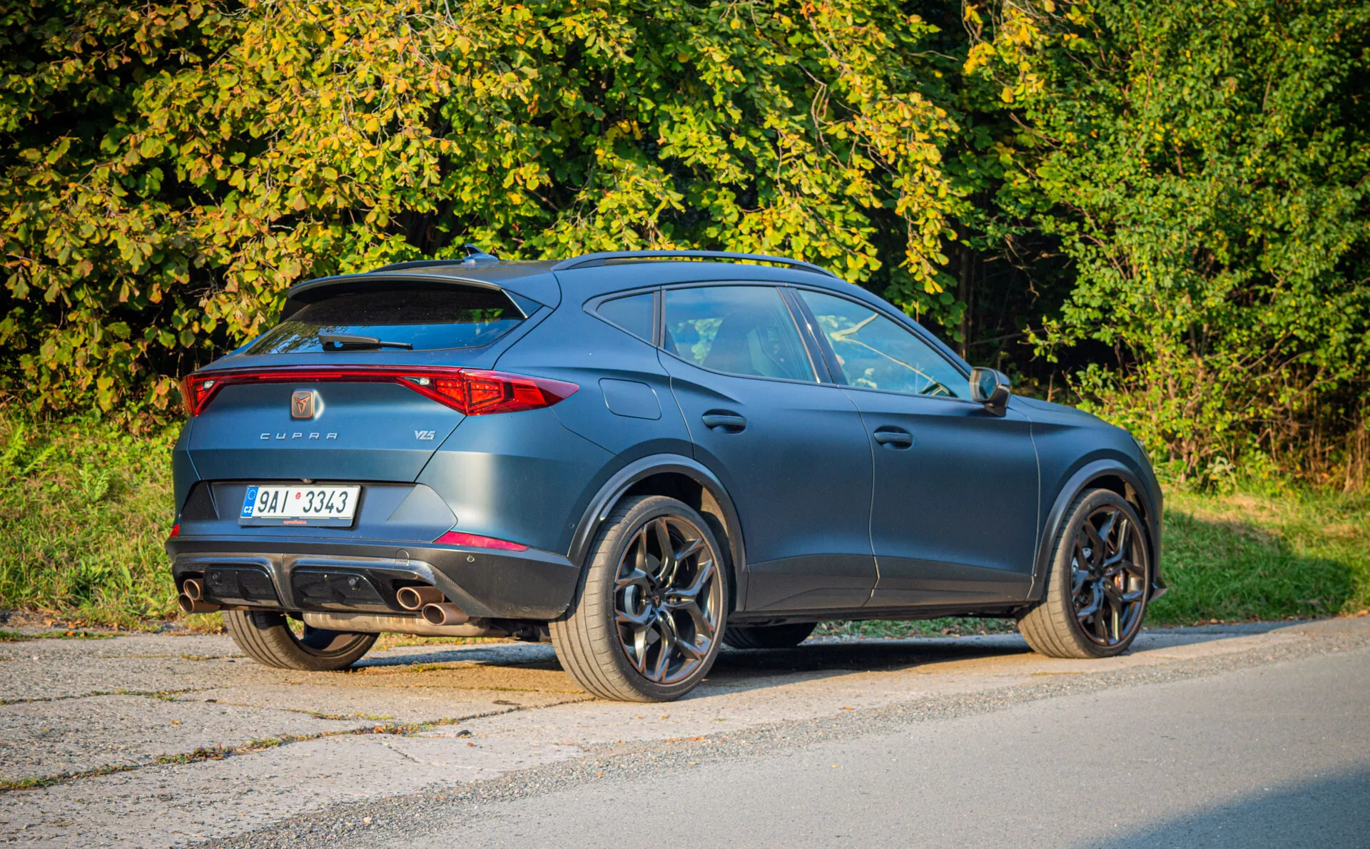 Moderne SUV crossover Cupra Formentor 2020 gris foncé mat noir garé sur l'asphalte, montrant vue arrière trois quarts accentuant design type coupé, aérodynamique sportive, feux arrière LED, aileron arrière, doubles échappements et grandes roues en alliage dans un cadre suburbain